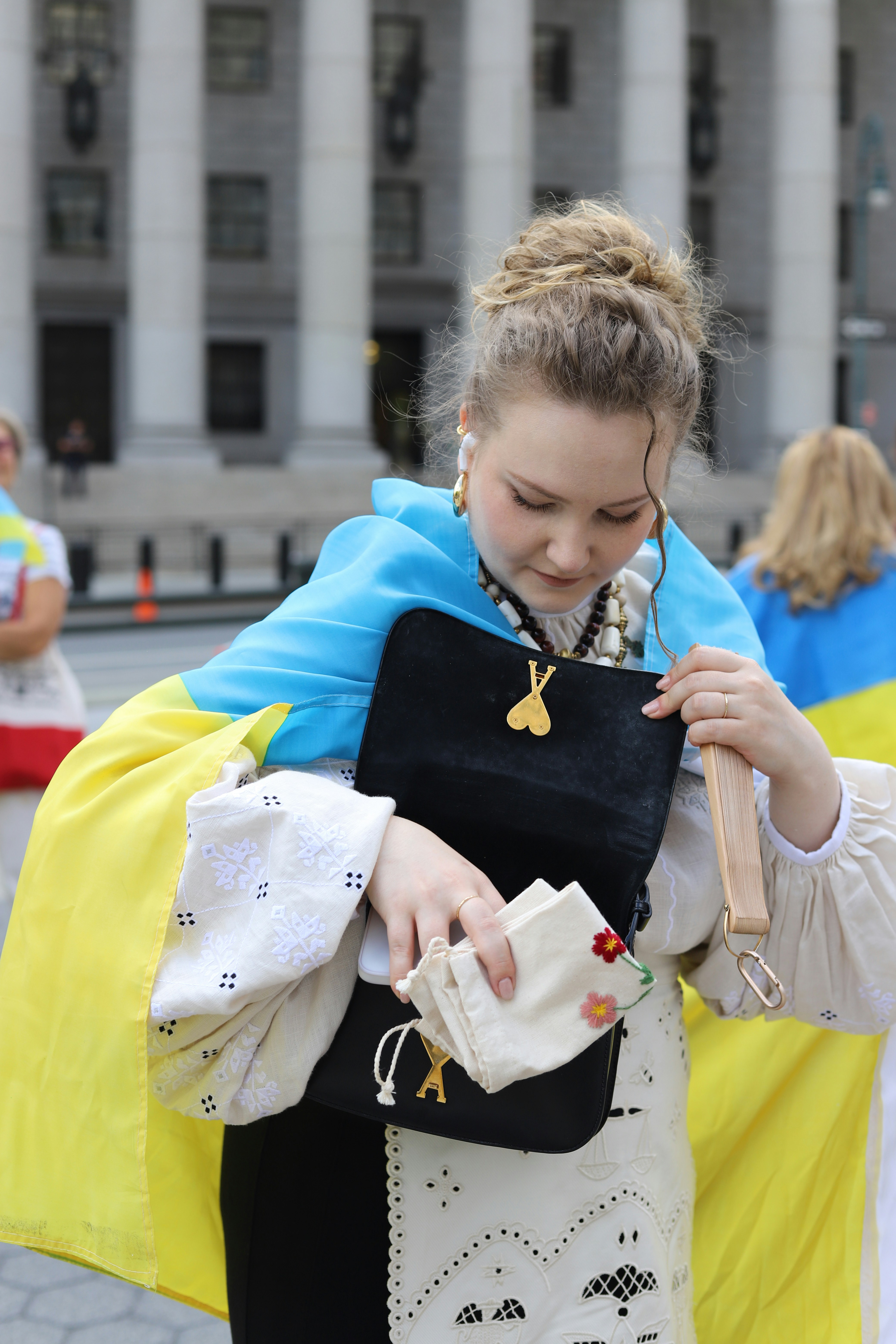 A woman in a traditional embroidered blouse with a Ukrainian flag draped over her shoulders