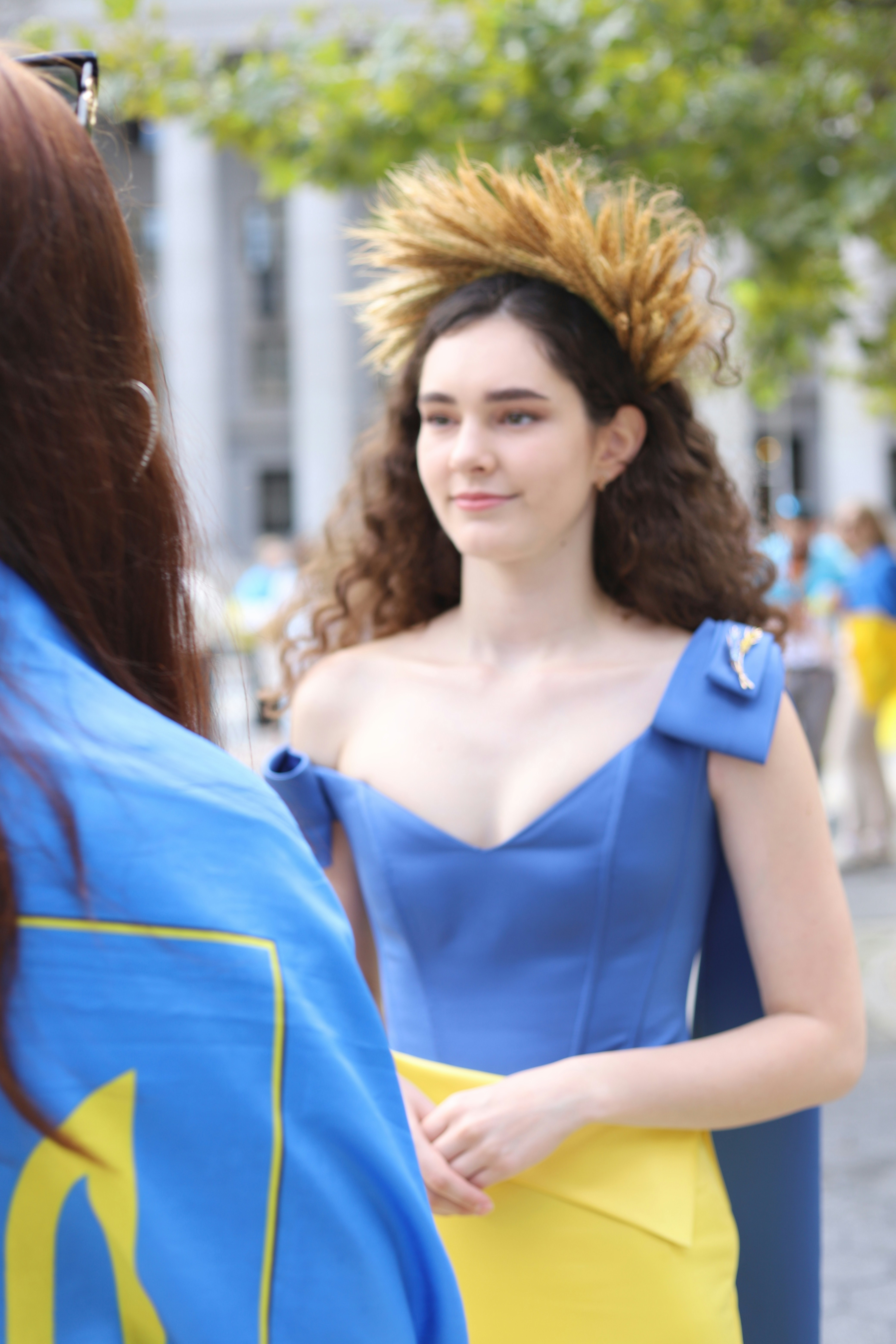 A woman with curly hair wearing a wheat crown and blue dress outdoors