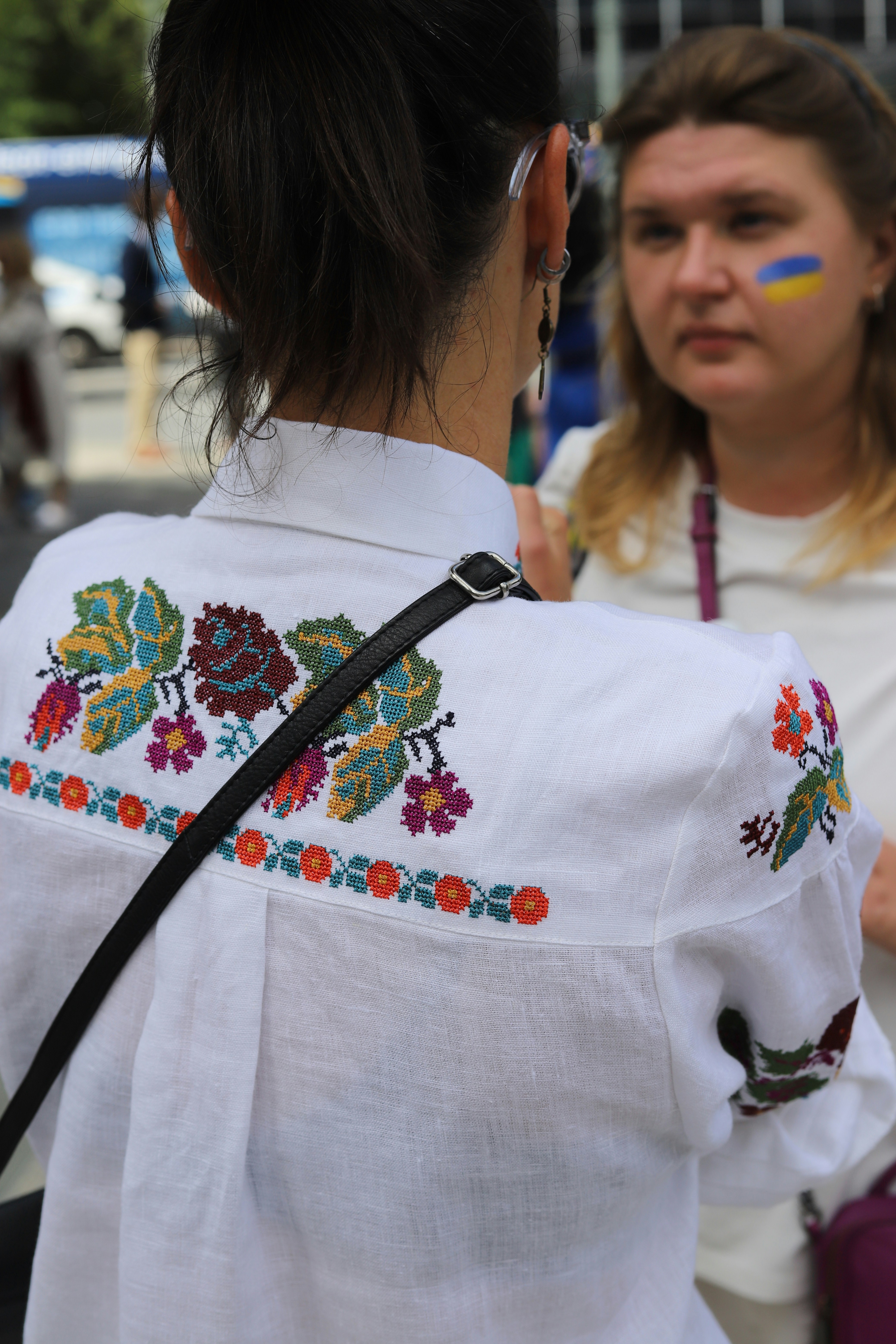 A person wearing a white embroidered shirt with a black shoulder strap