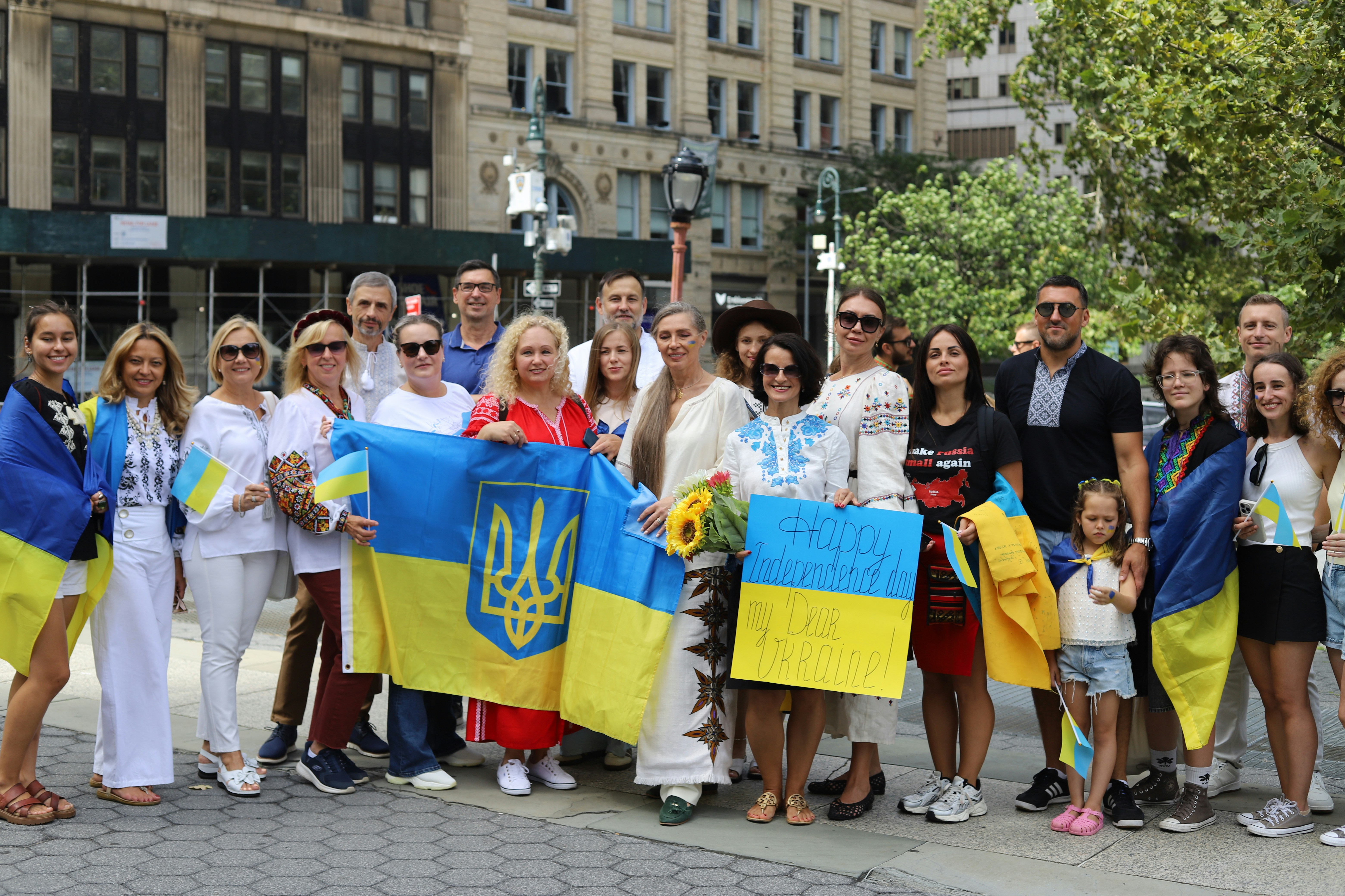 A group of people holding Ukrainian flags and a sign in a city park