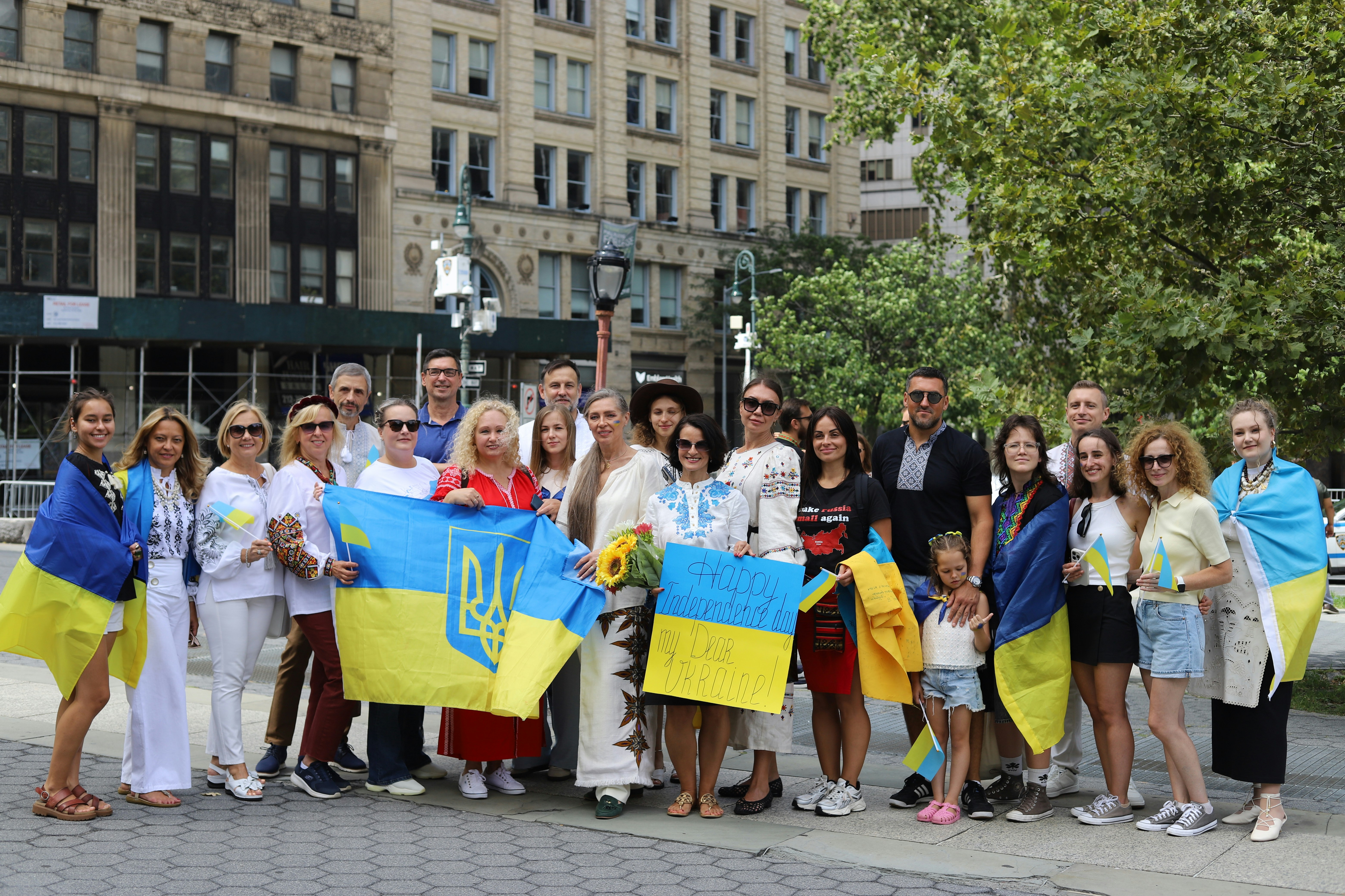 A group of people holding Ukrainian flags and a sign in a city park