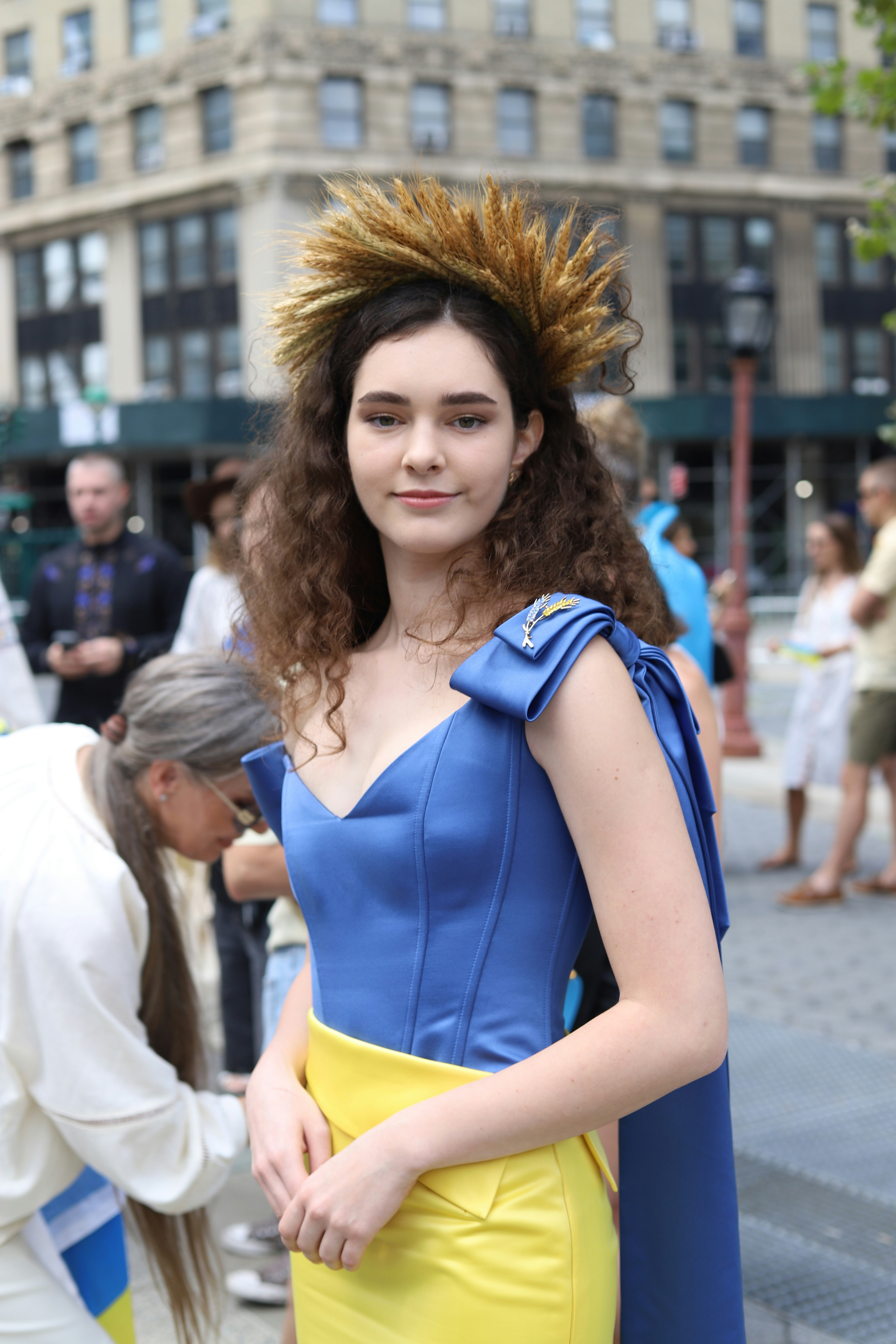A woman wearing a blue and yellow dress and a wheat crown outdoors