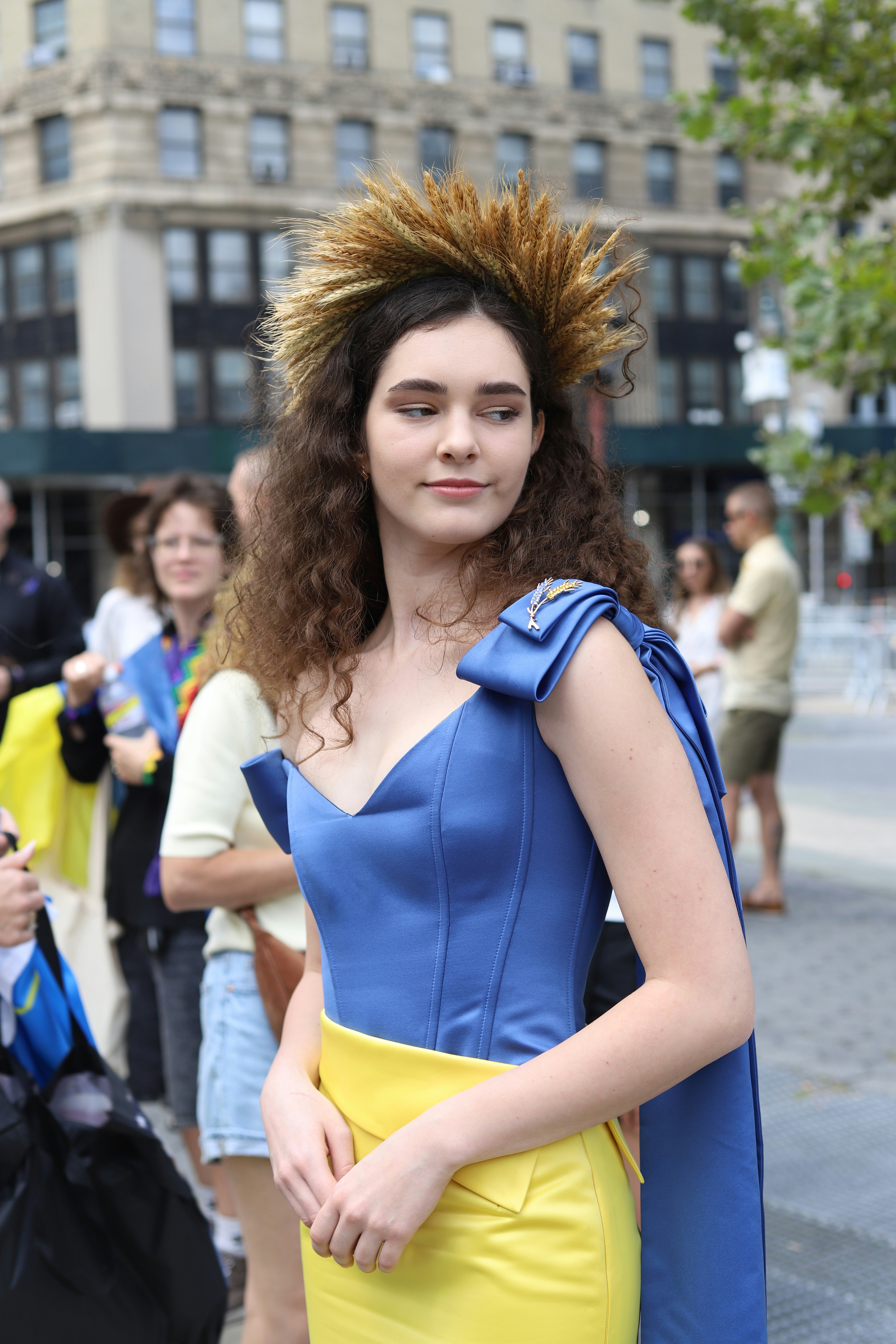 A woman wearing a blue dress and a wheat crown on a city street