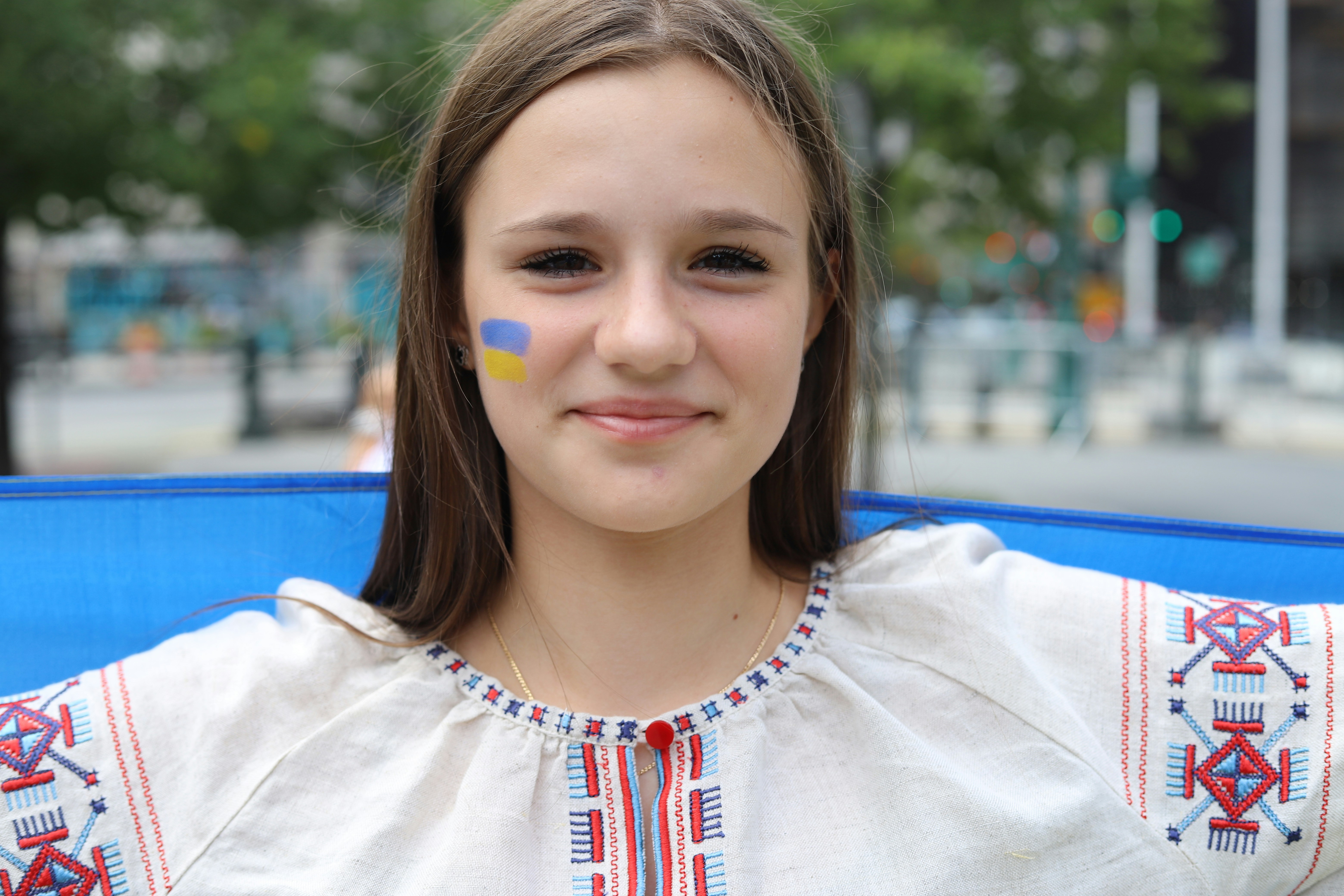 A young woman wearing a traditional embroidered shirt with blue and yellow face paint