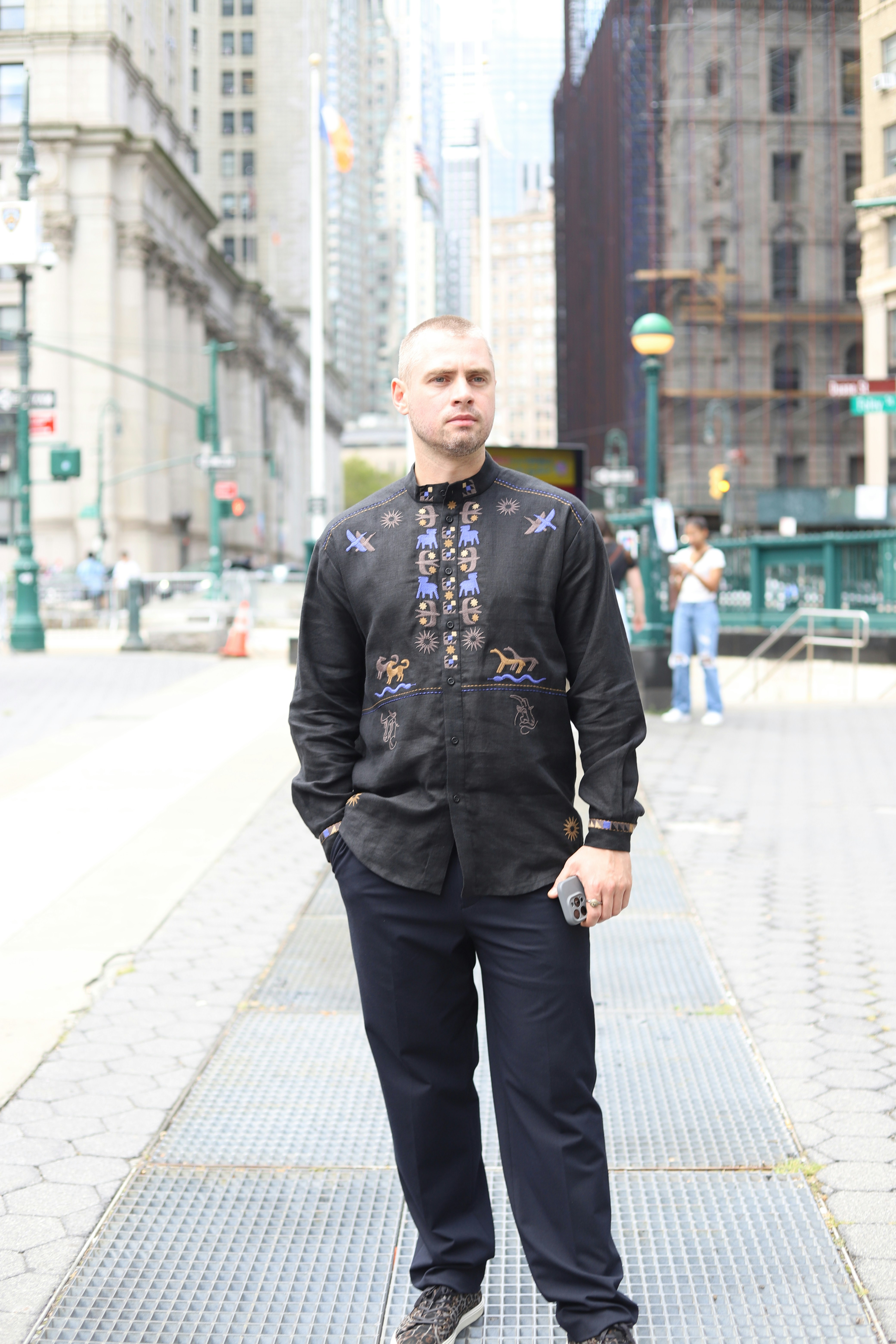 A man in a black embroidered shirt on a city sidewalk in New York