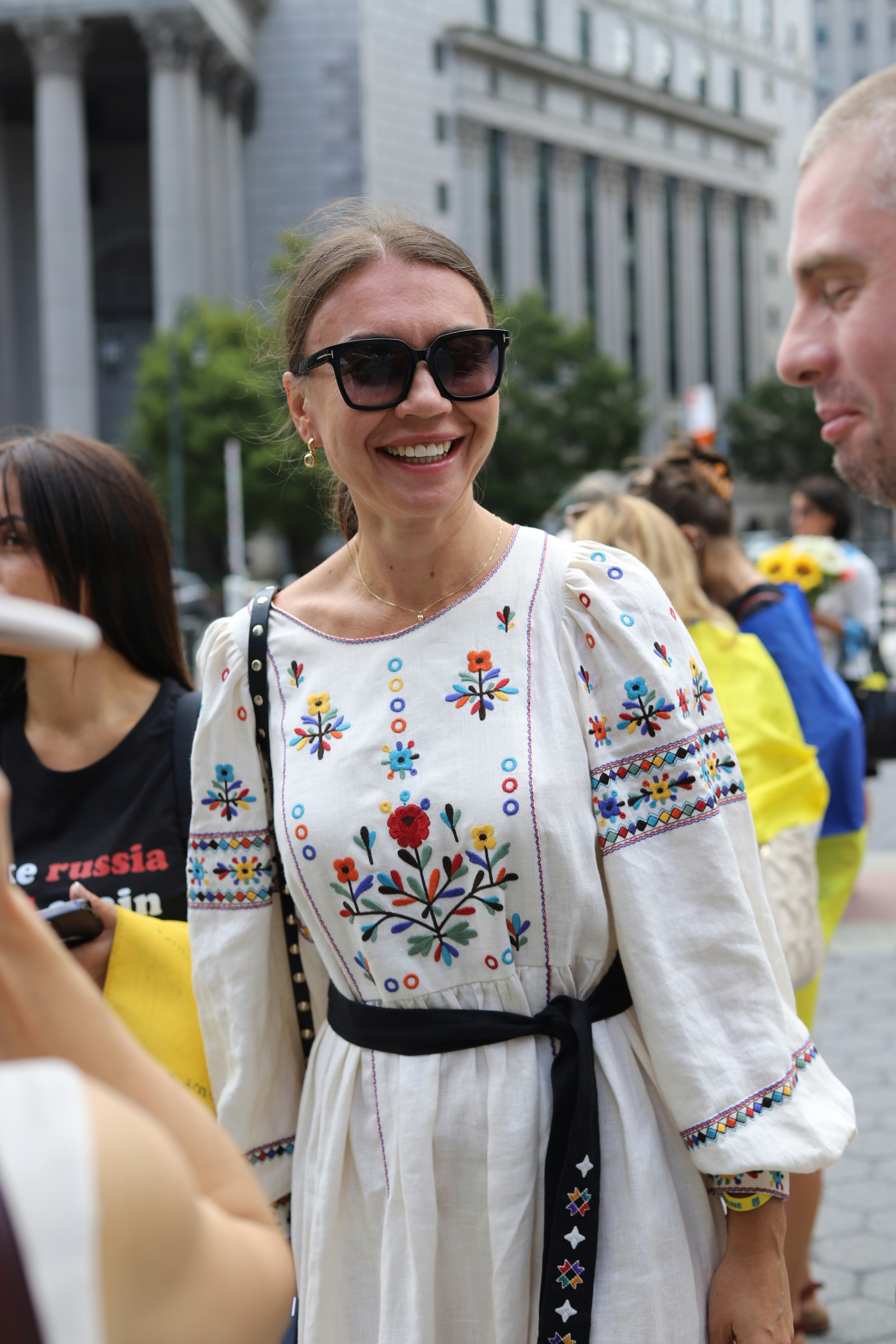 A smiling woman wearing a white embroidered dress with a black waist tie