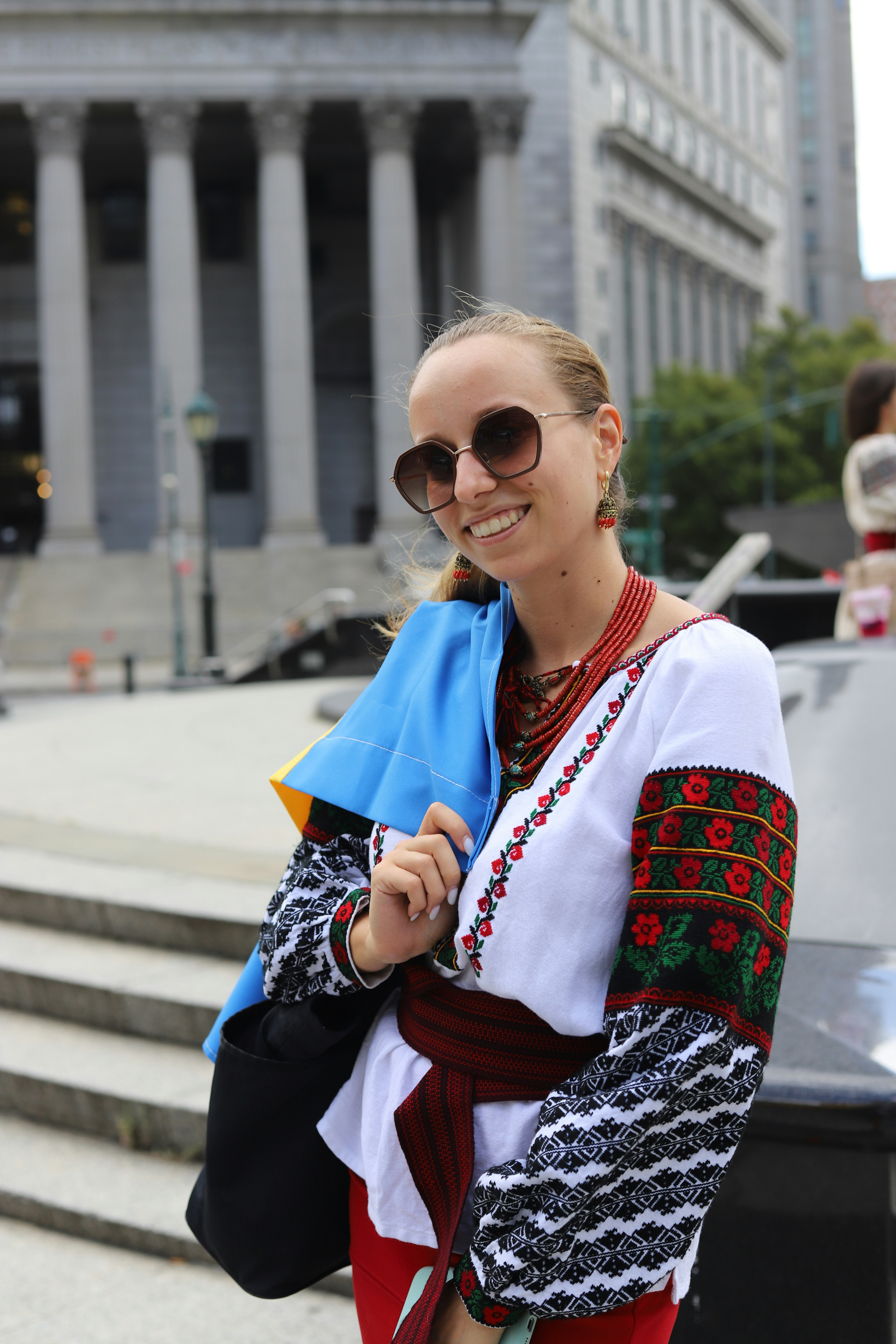 A woman wearing a traditional embroidered vyshyvanka shirt and sunglasses in front of a building