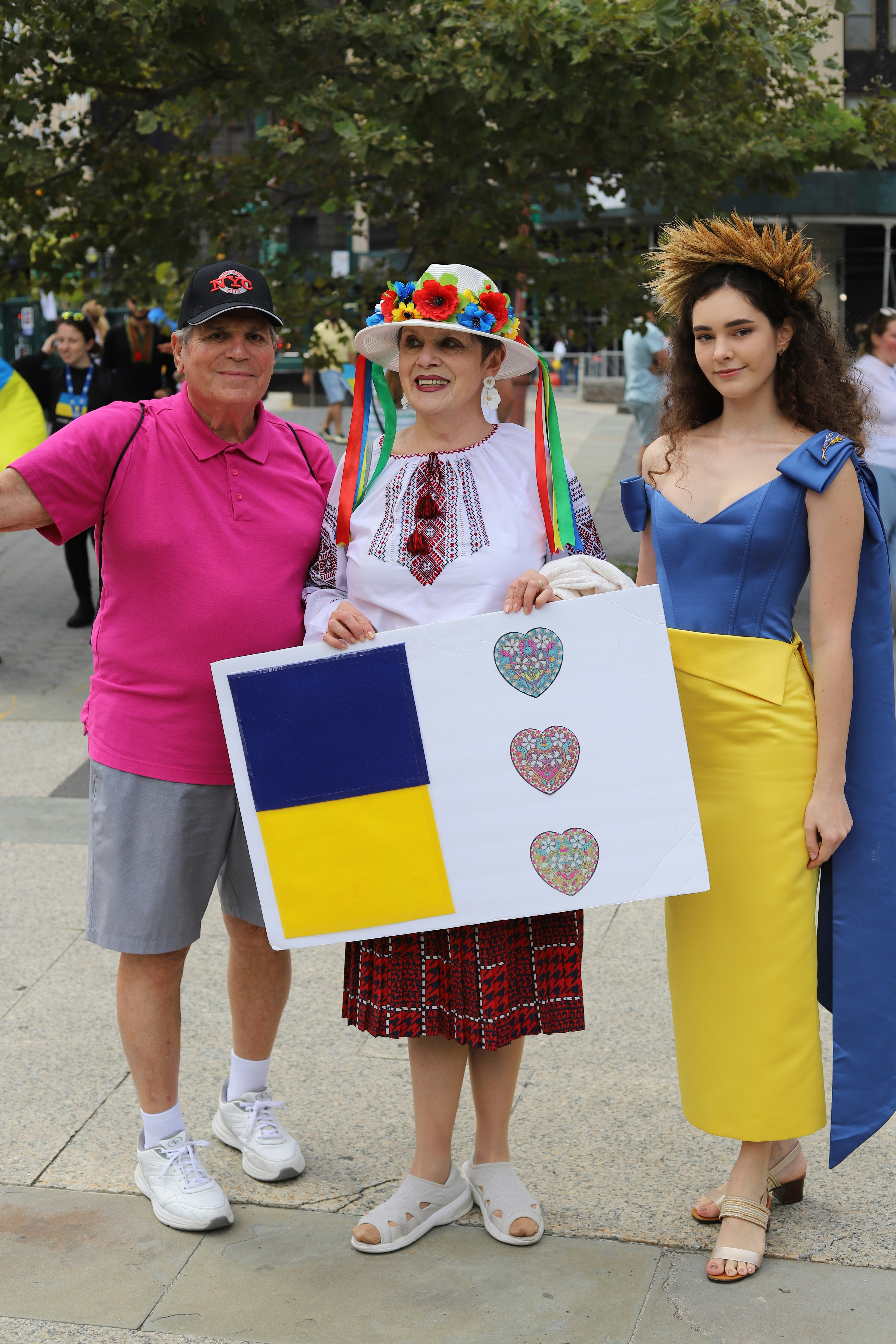 Three people holding a sign with a Ukrainian flag and hearts in a park