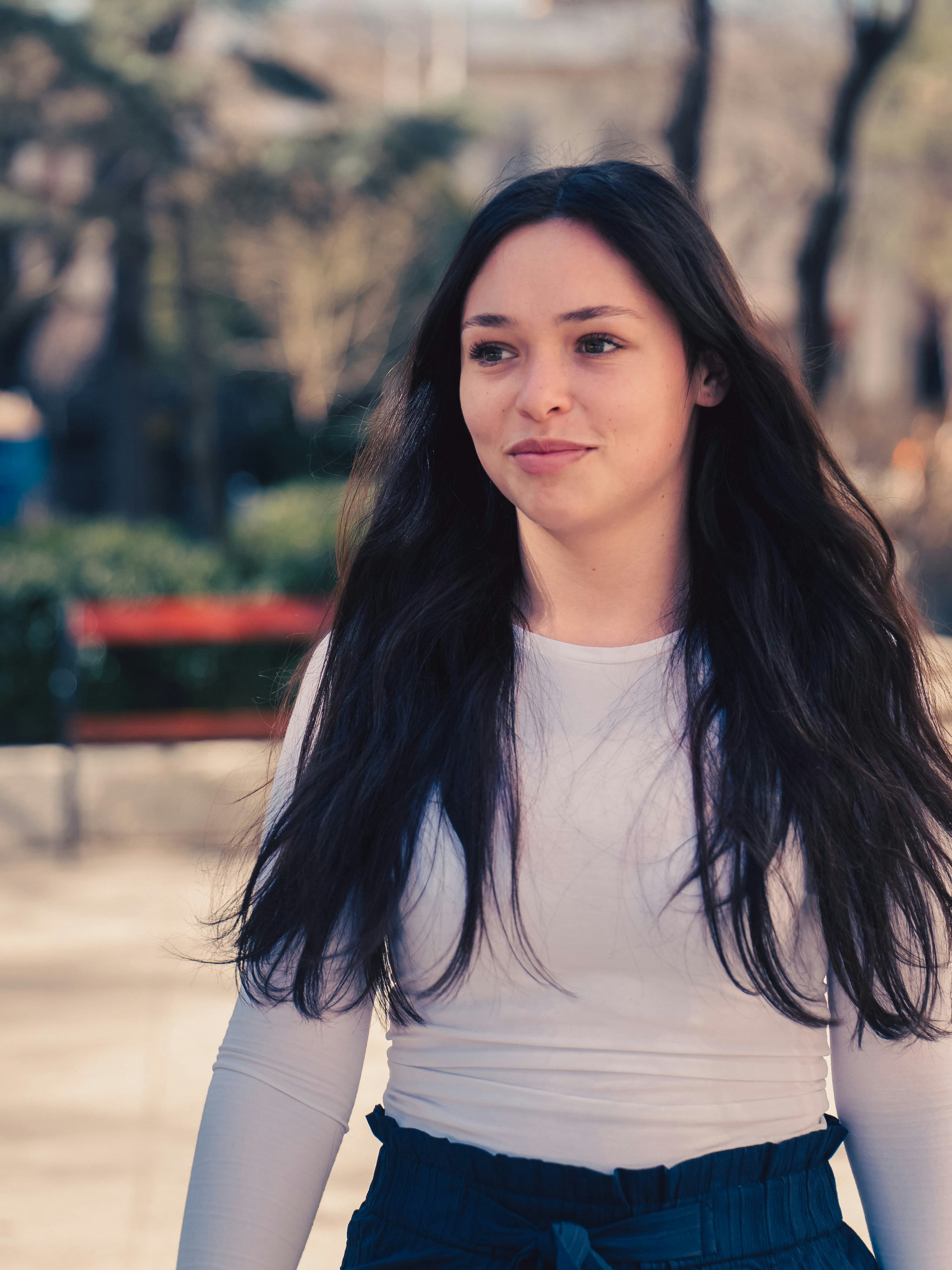 A young woman with long dark hair wearing a white long-sleeved shirt outdoors