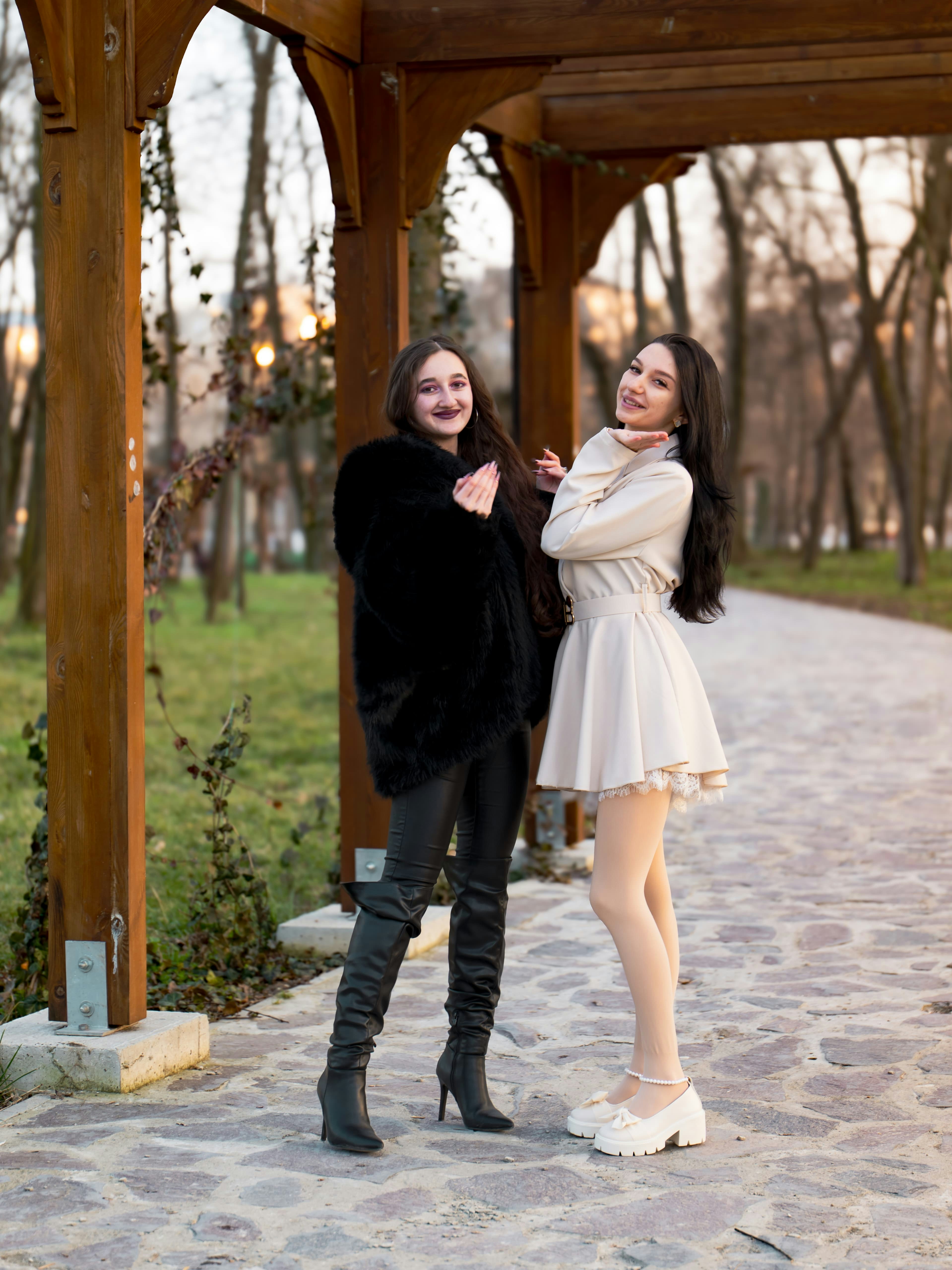 Two women in winter coats posing under a wooden pergola on a stone path