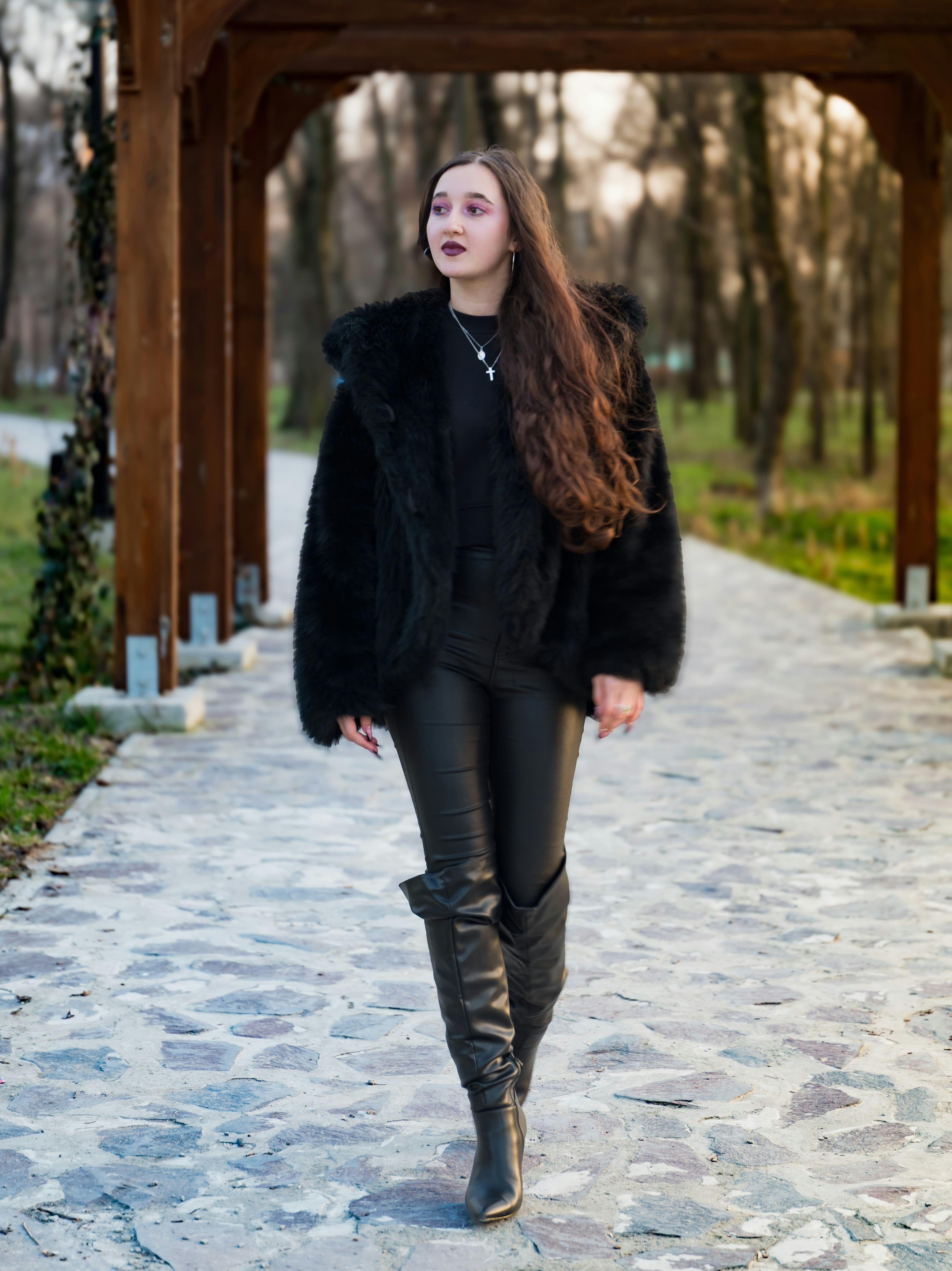 A woman walking along a stone path beneath a wooden pergola in a park