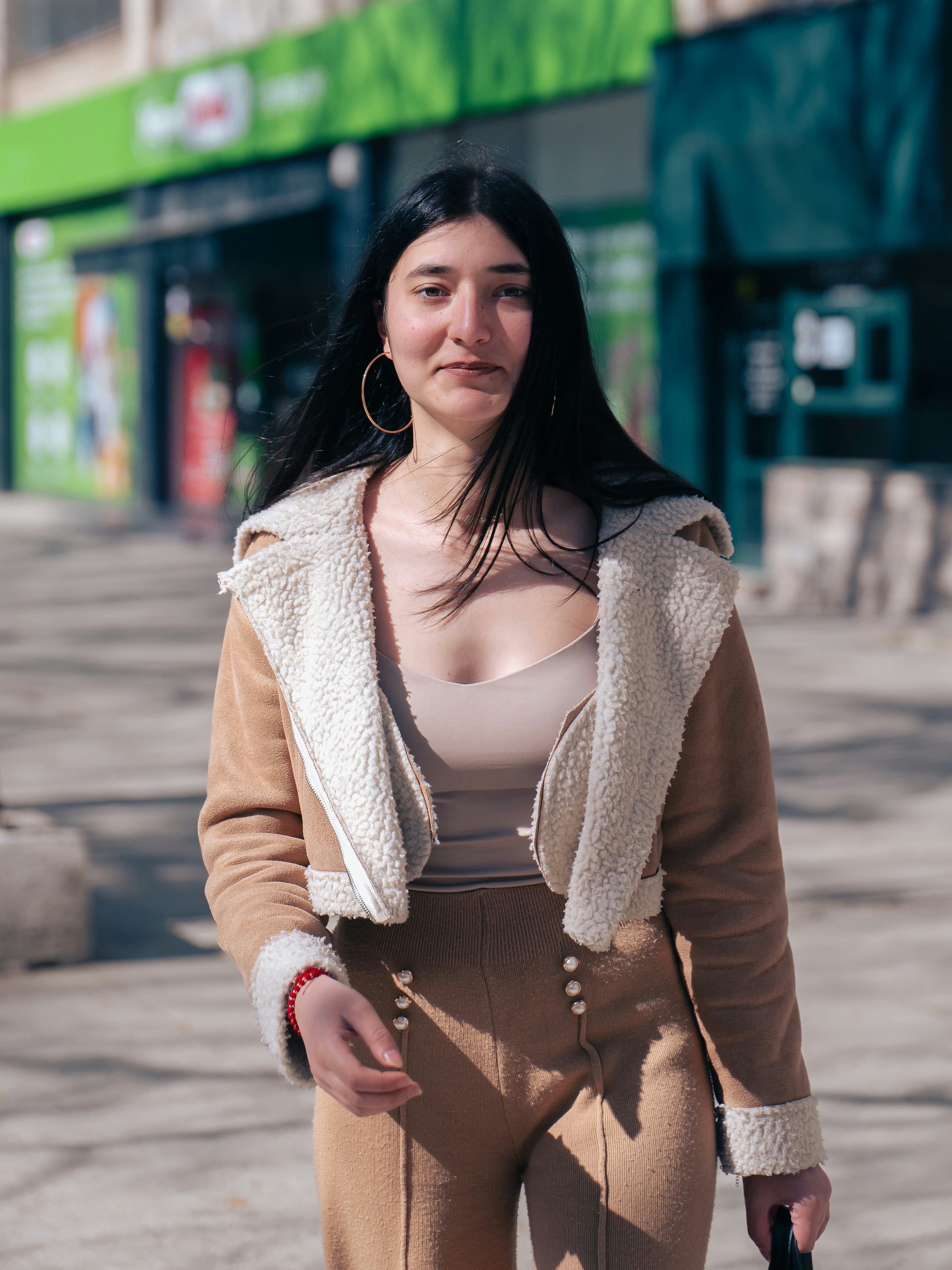 A woman with long dark hair wearing a tan shearling jacket on a city street