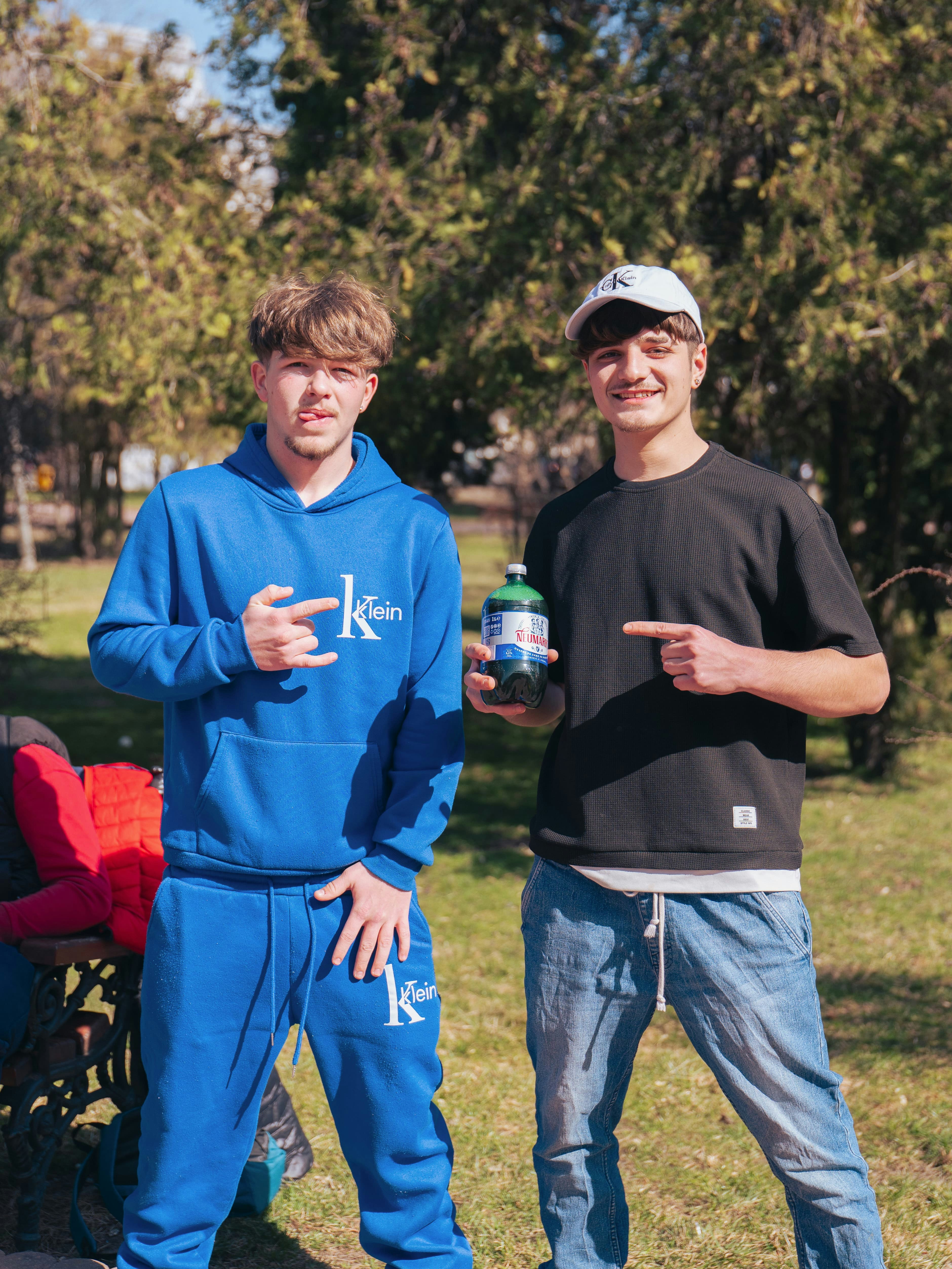 Two young men in a sunny park, one holding a bottle