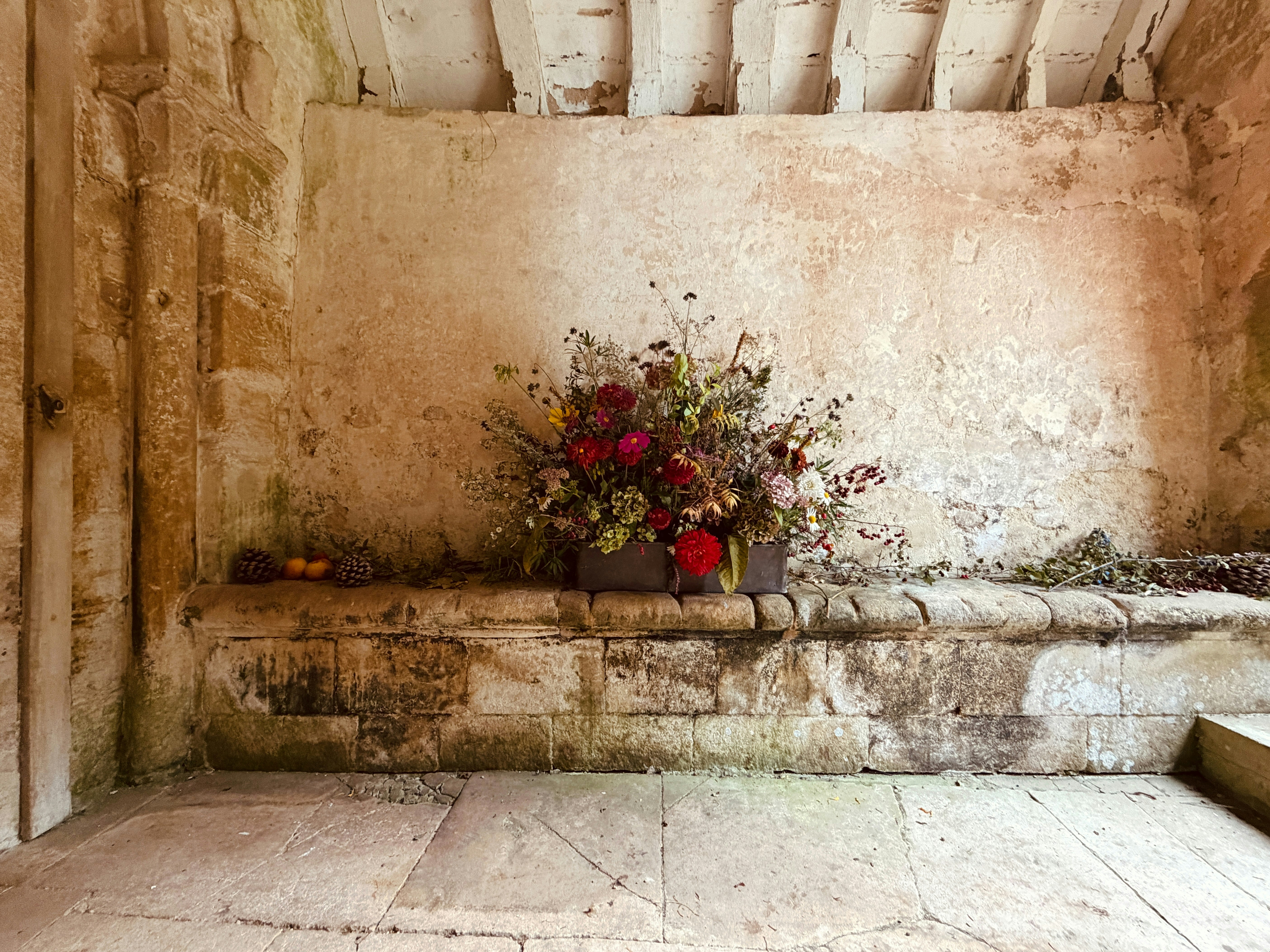 A large floral arrangement on a weathered stone bench against a rustic wall