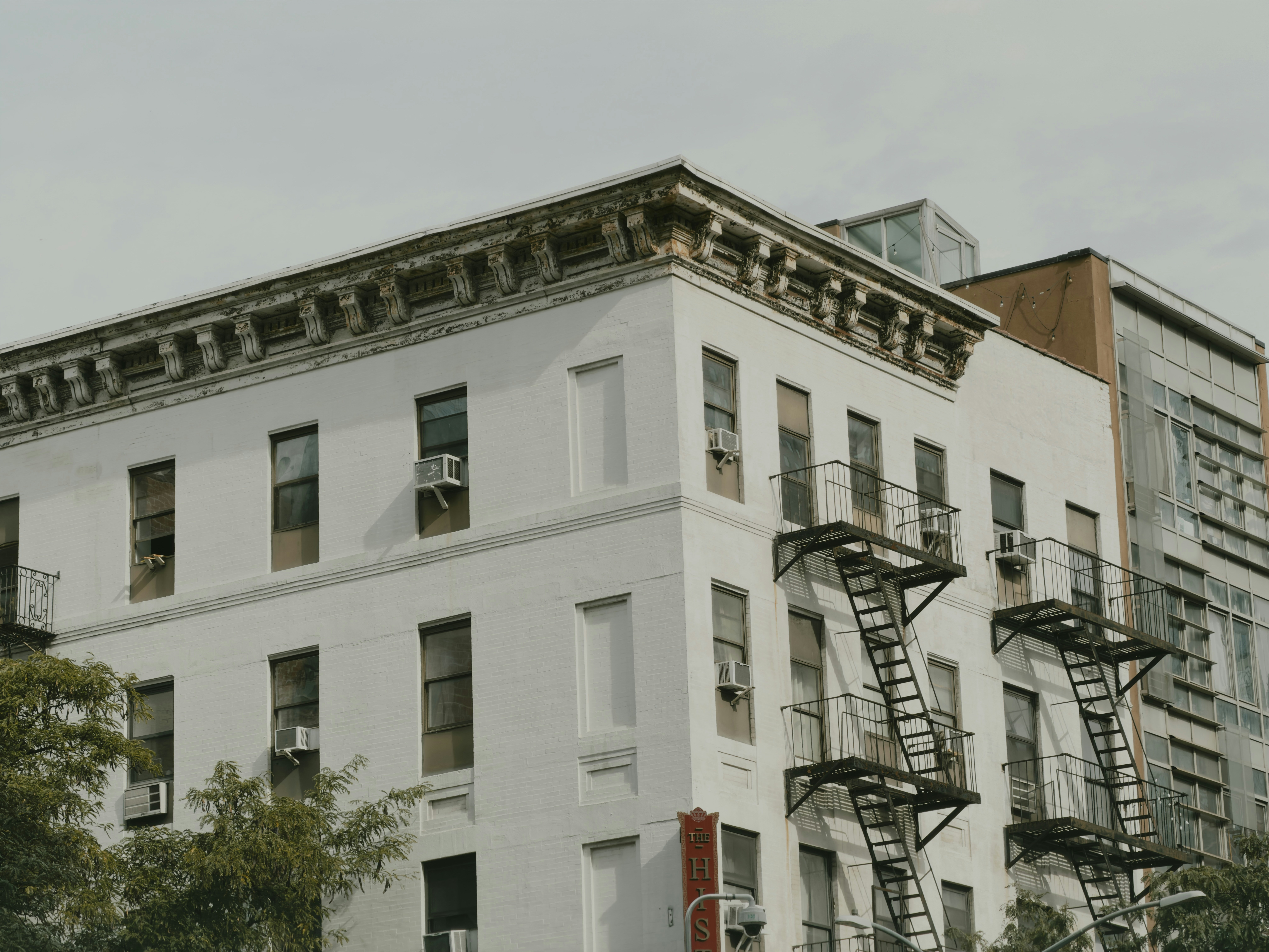 A white brick apartment building with black metal fire escapes on a cloudy day