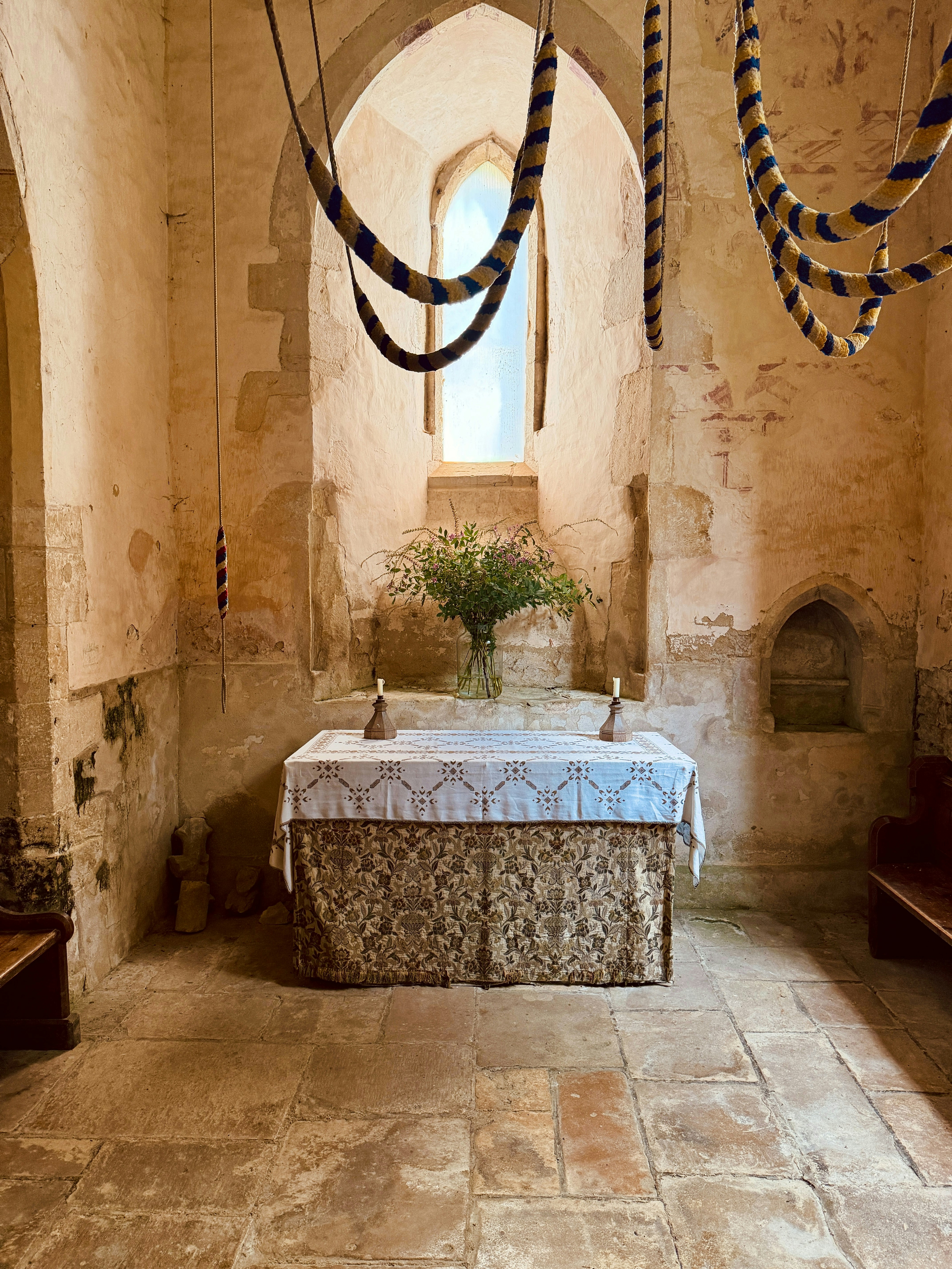 An altar with a patterned cloth and candles in a stone church interior