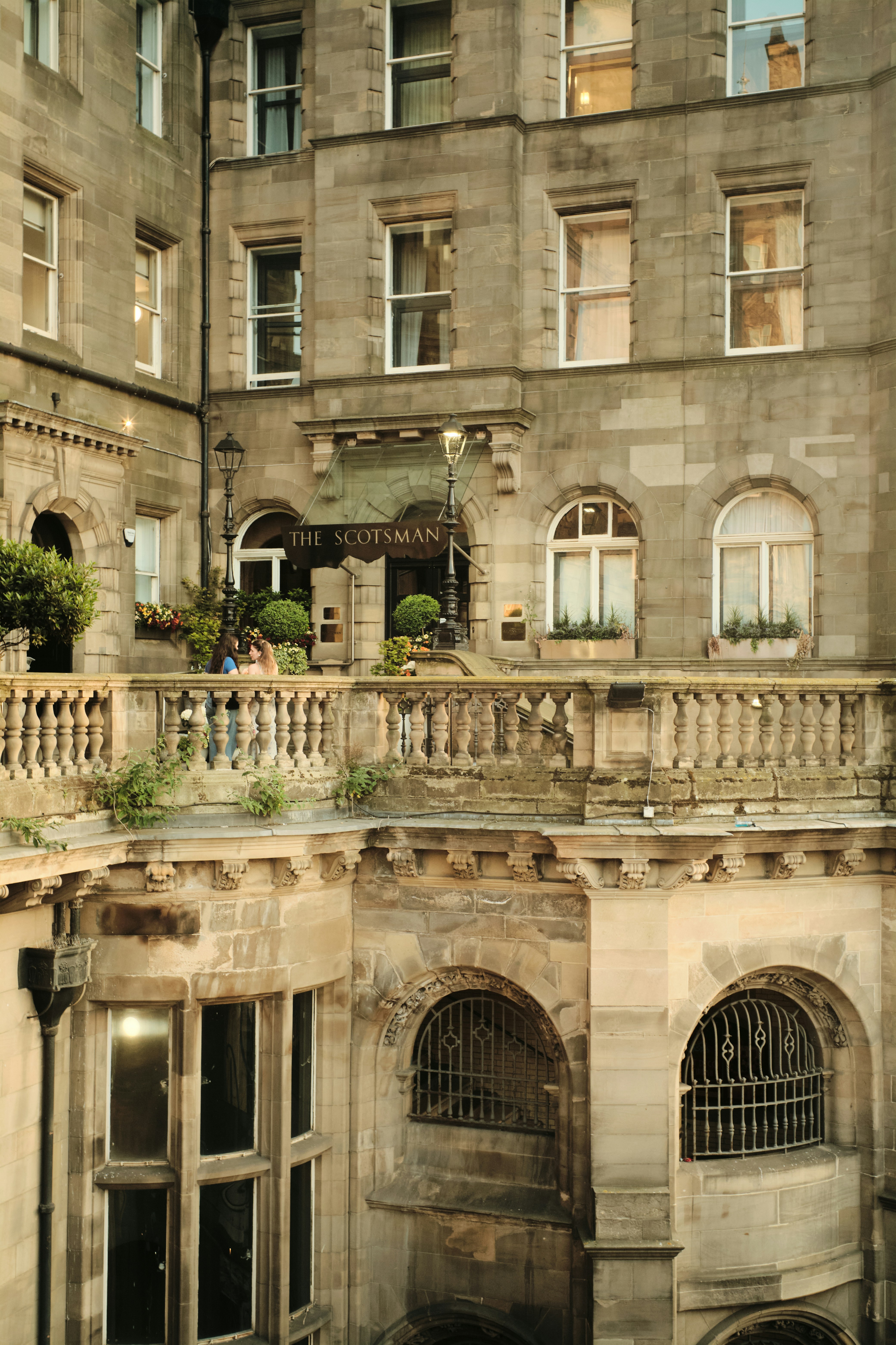 Two people on a stone balcony in front of The Scotsman hotel in Edinburgh