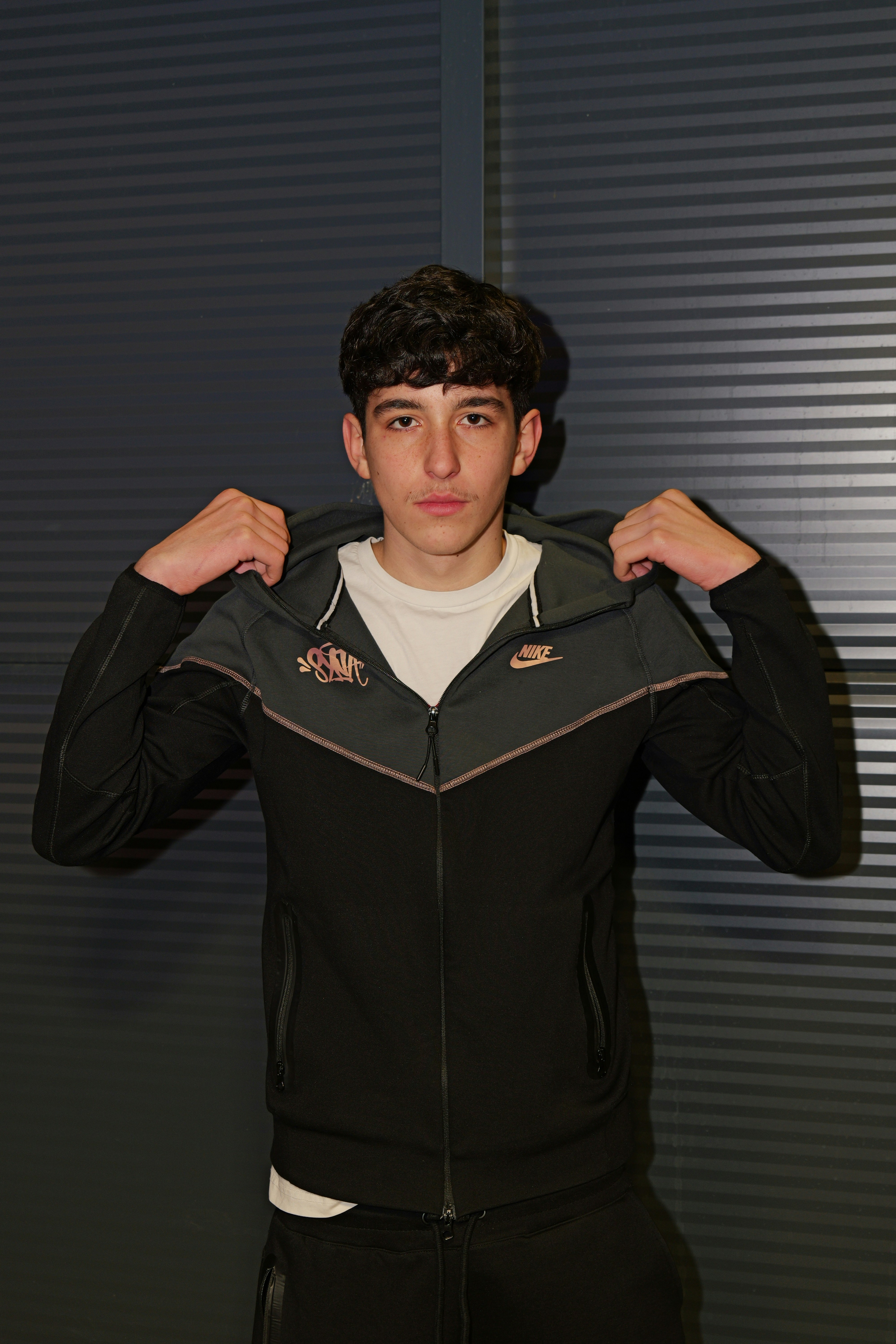 A young man wearing a black and grey zip-up hoodie over a white shirt