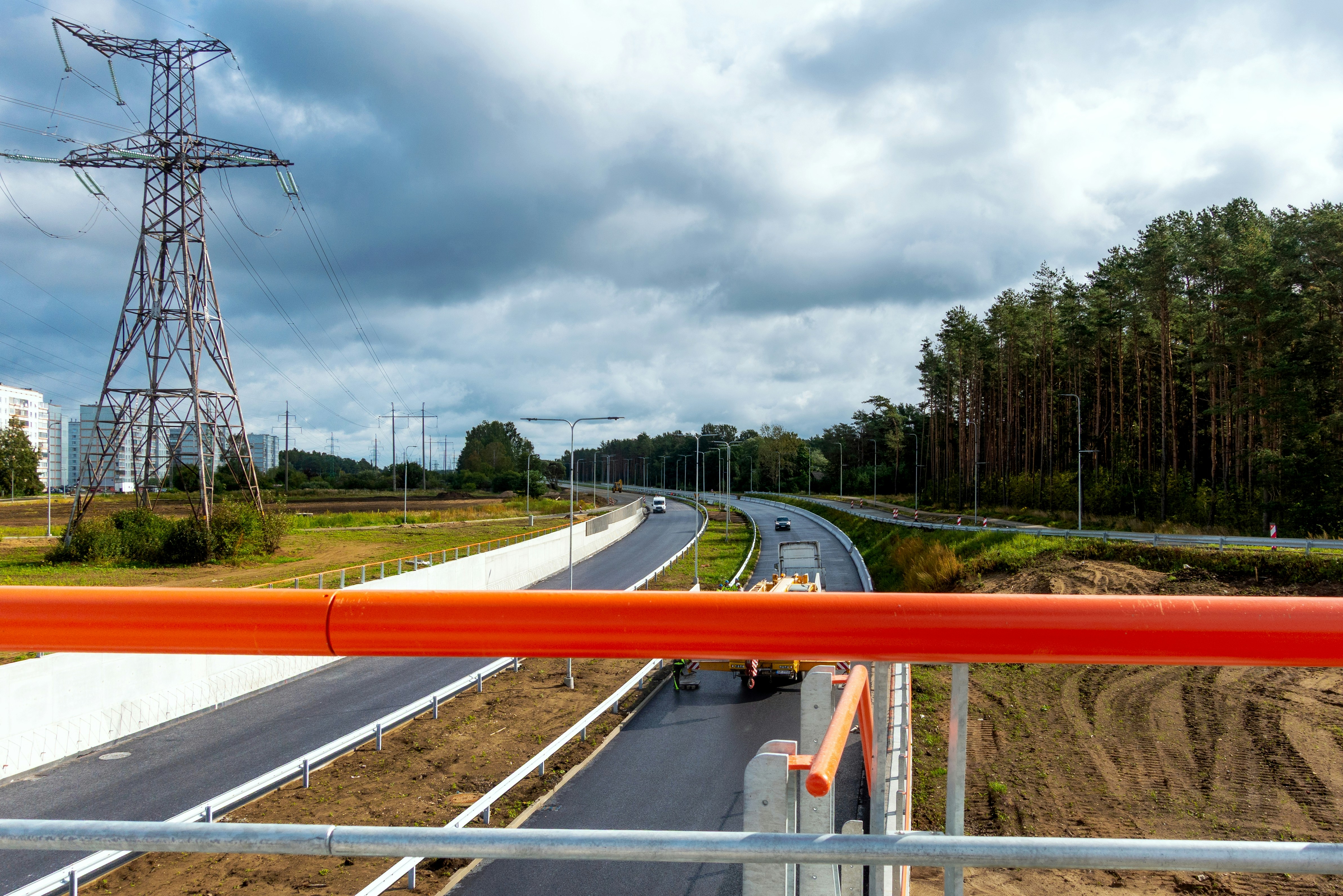 A highway curving through a landscape with a tall electricity pylon and pine trees