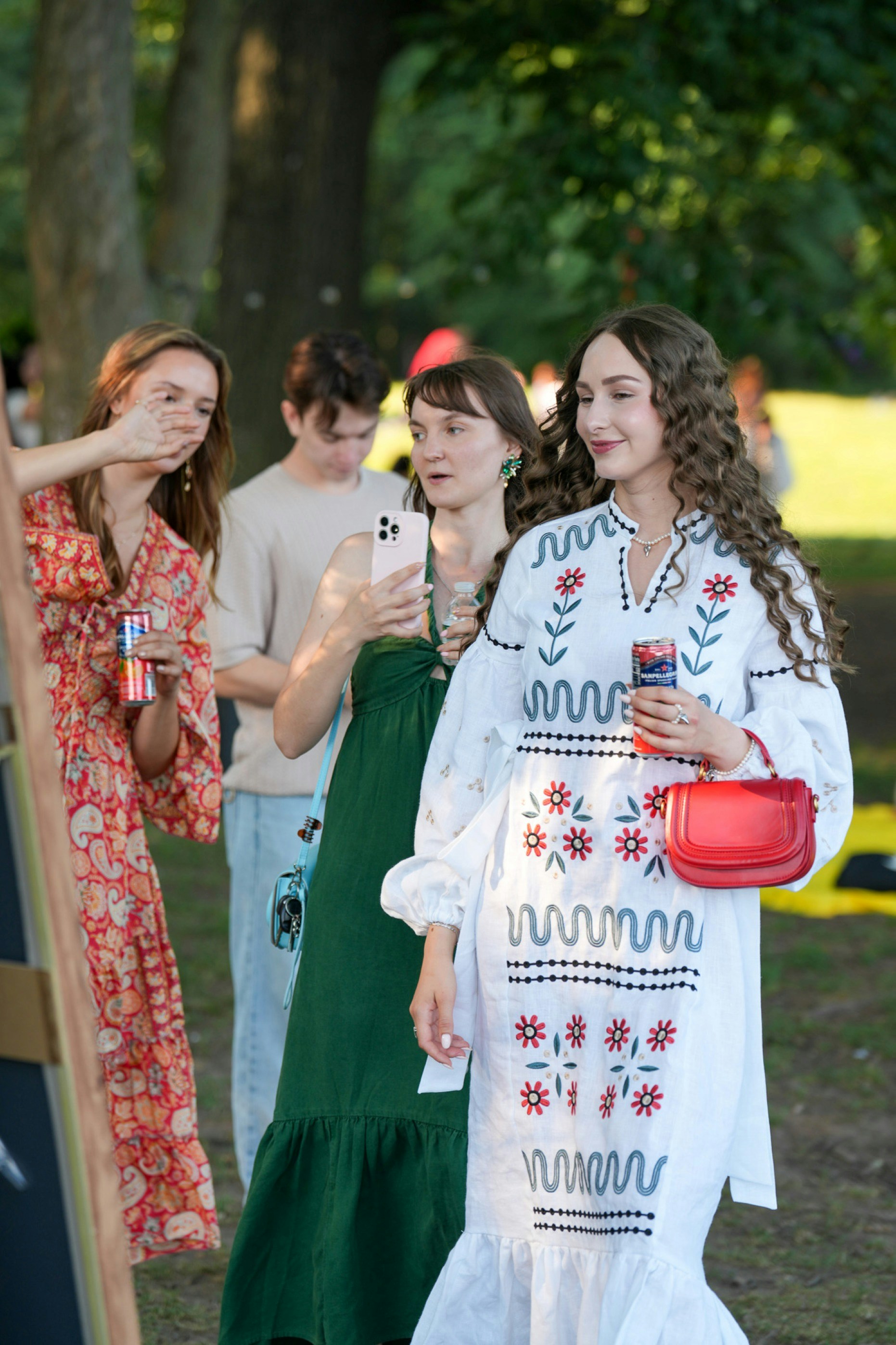 A group of people in a park with one woman holding a red bag