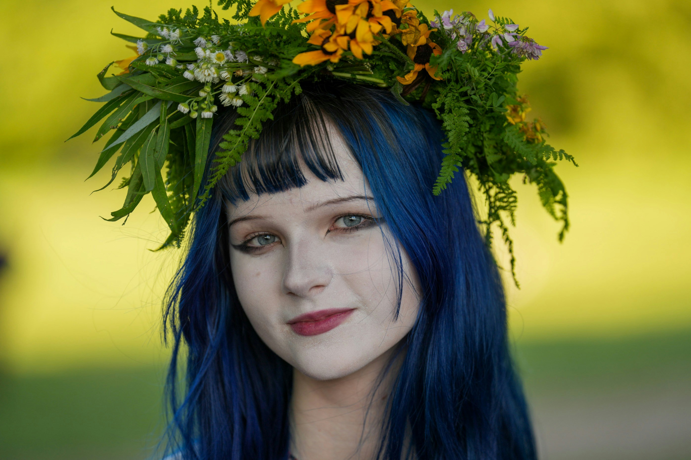 A person with blue hair wearing a crown of wildflowers and ferns