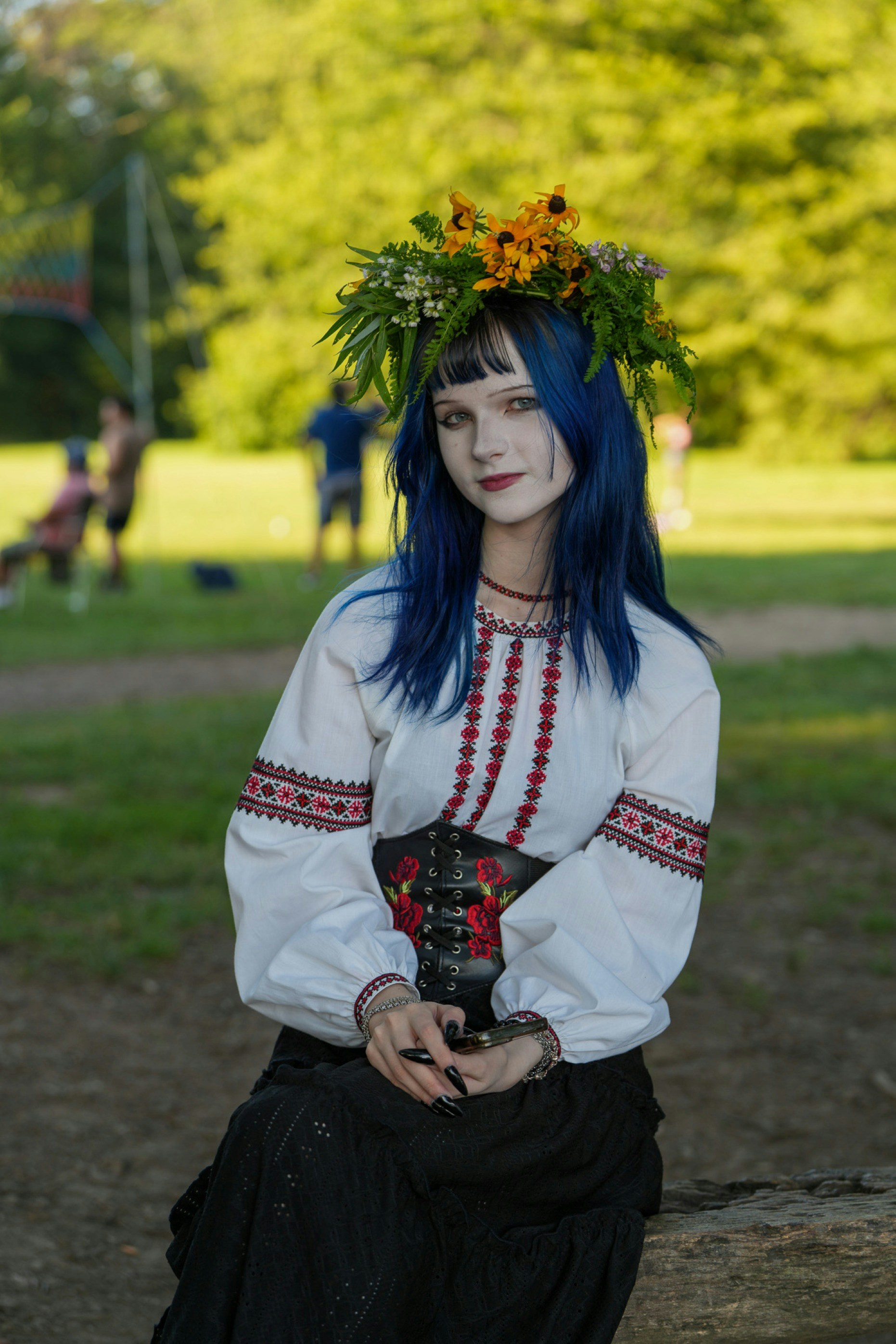 A person with blue hair and a flower crown wearing a traditional embroidered blouse