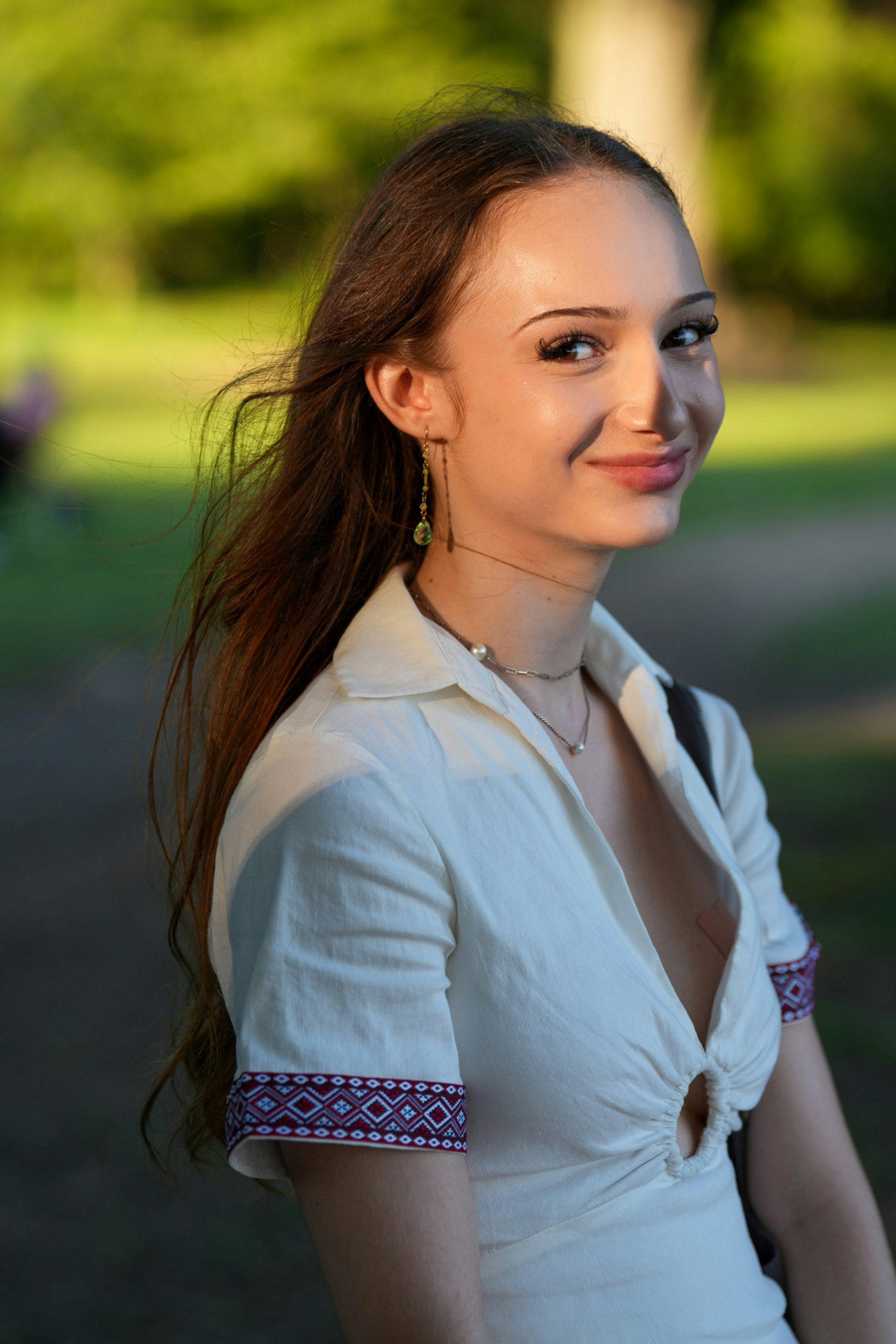 A woman with long brown hair in a white shirt outdoors in golden light