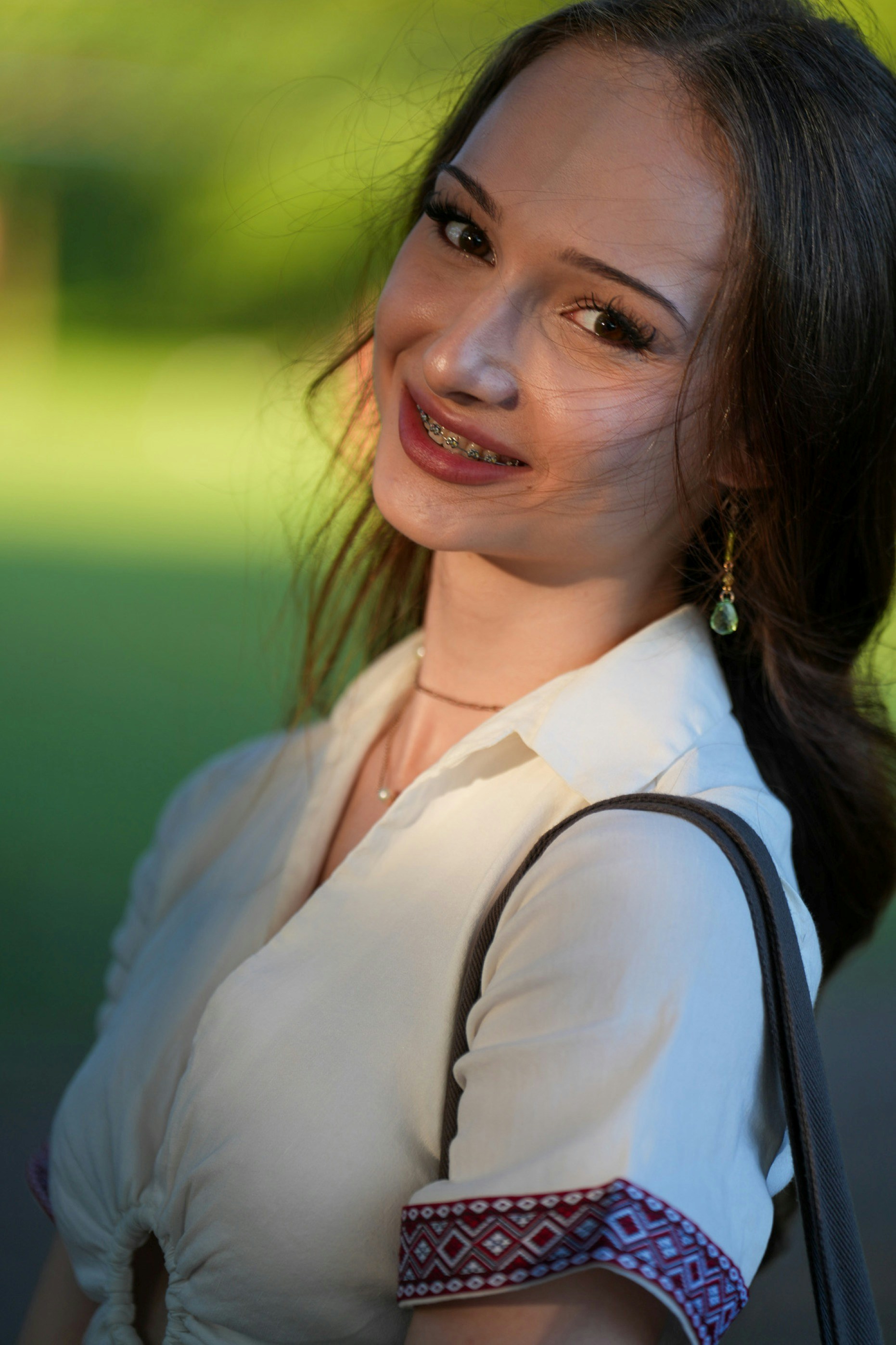 A smiling woman with braces wearing a white shirt with patterned sleeve cuffs