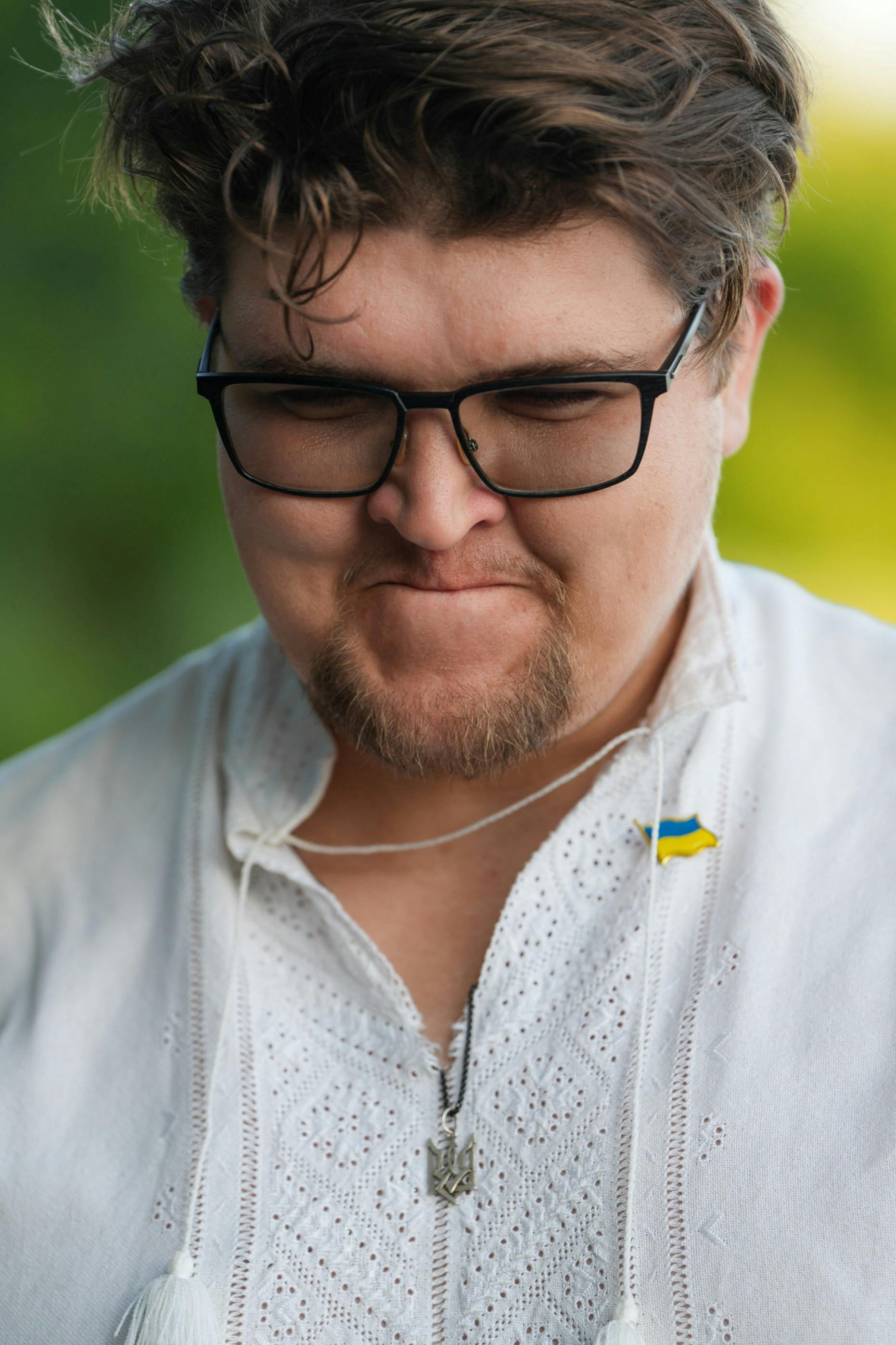 A person with glasses wearing a white embroidered shirt with a small Ukrainian flag pin