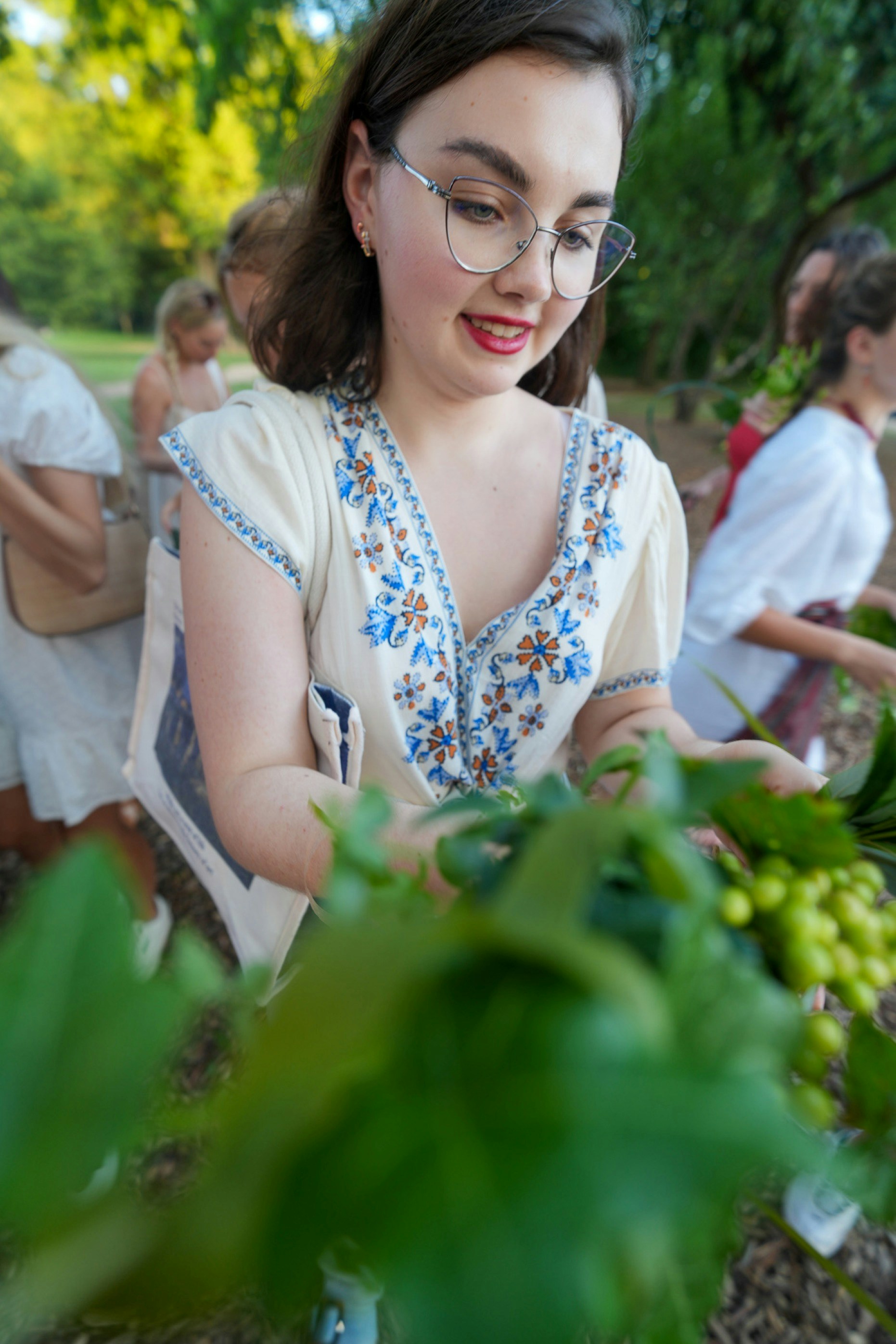 A woman in a white embroidered dress arranging green foliage in a park