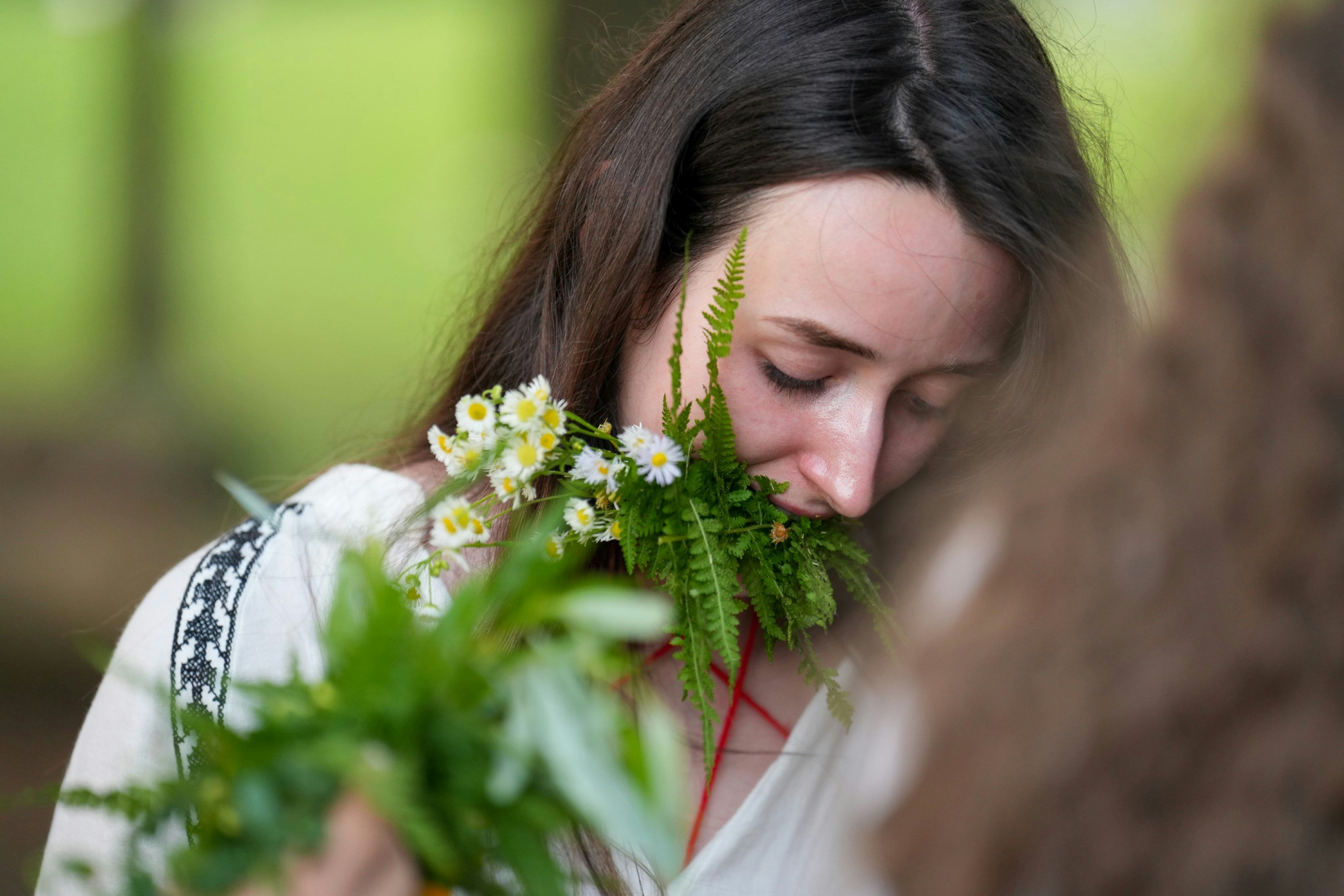 A woman holding a bundle of ferns and white daisies near her face