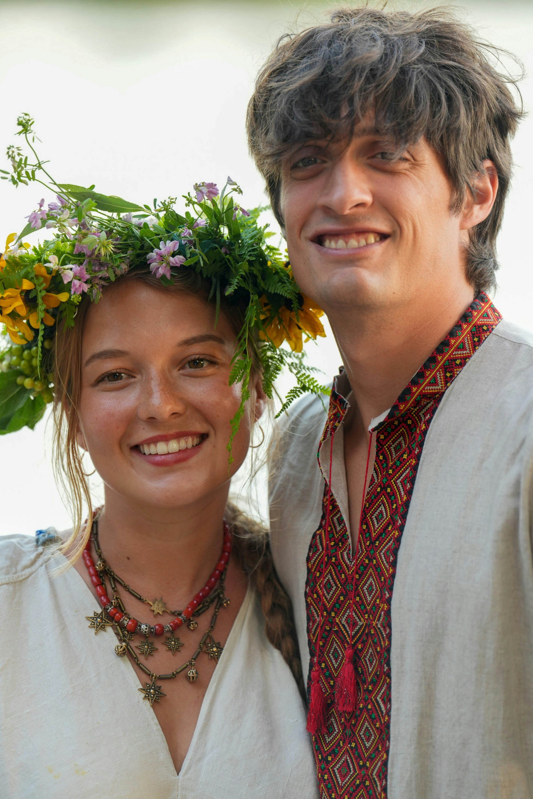 A smiling woman wearing a floral crown and a man in an embroidered shirt