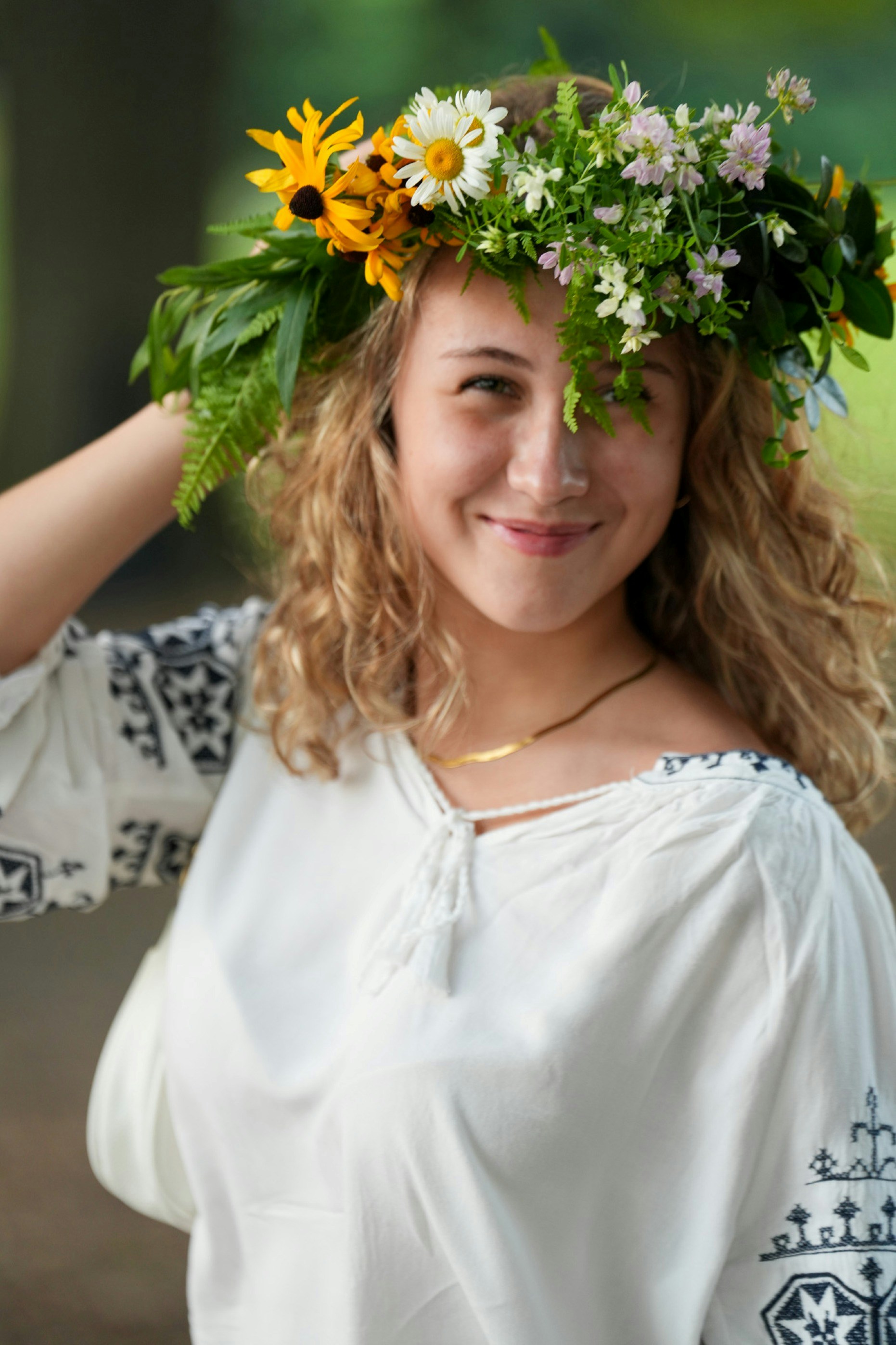 A young woman with curly blonde hair wearing a floral crown and embroidered blouse