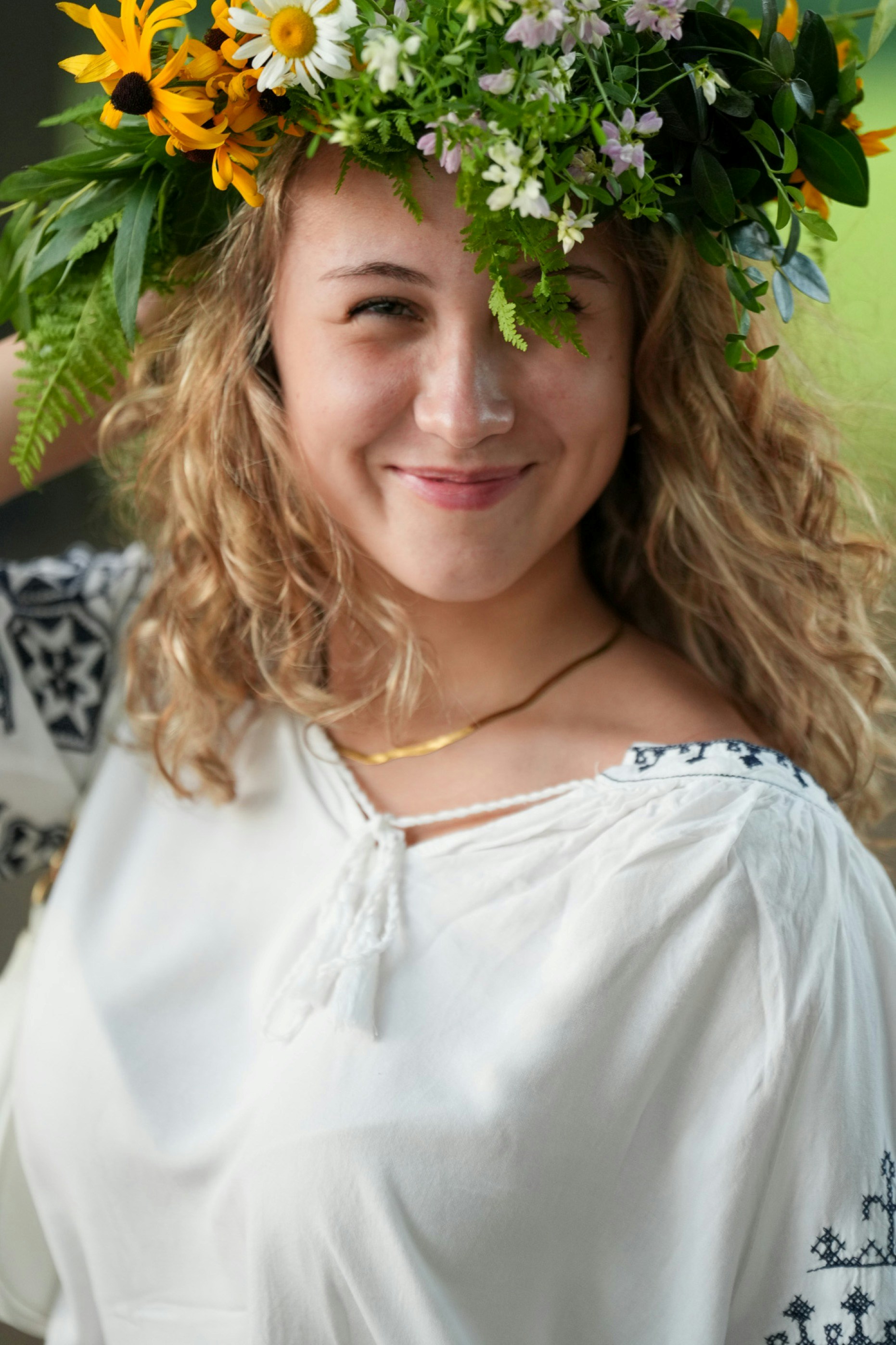 A smiling woman with curly blonde hair wearing a floral crown of wildflowers