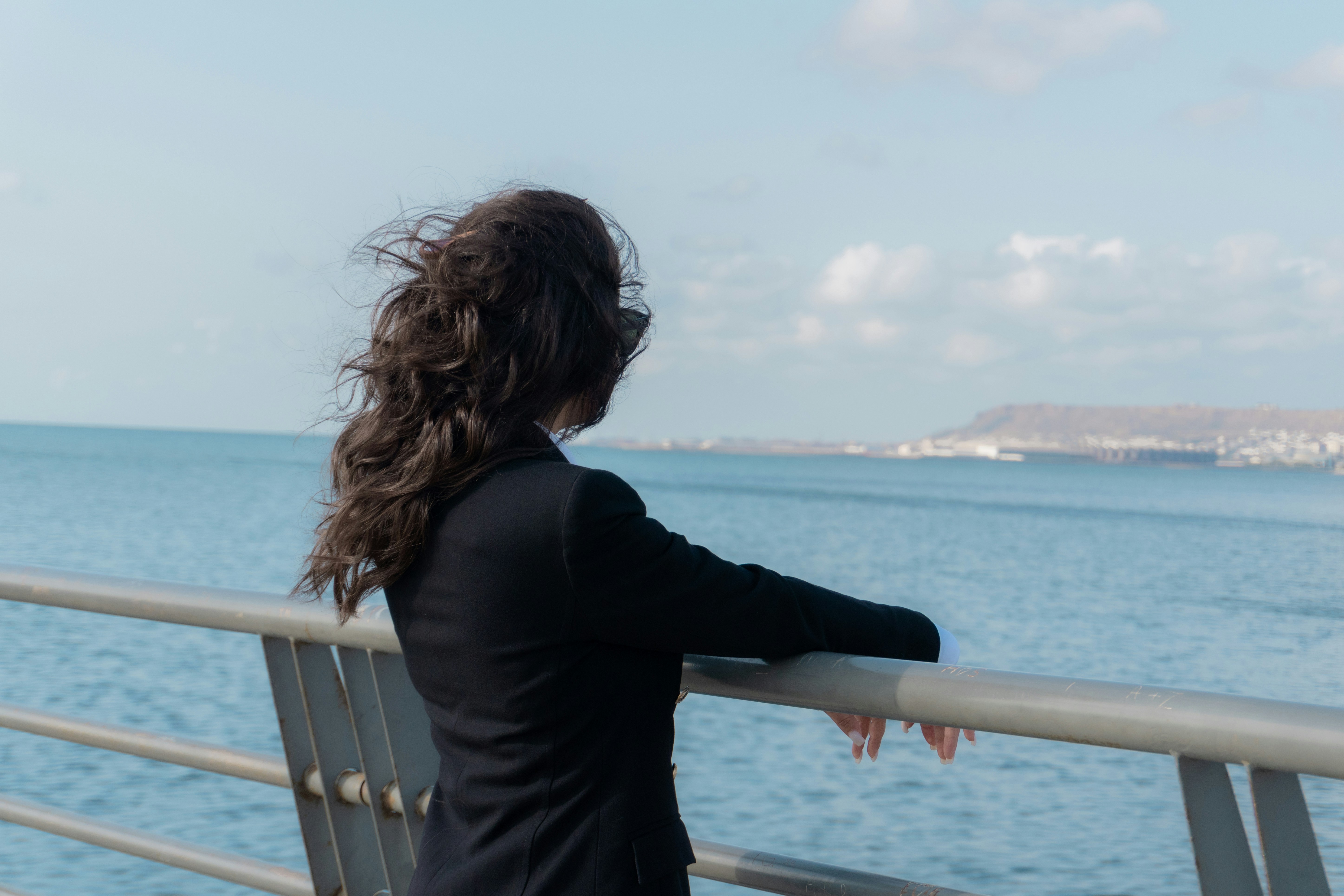 A woman in a black blazer looking out over the blue sea