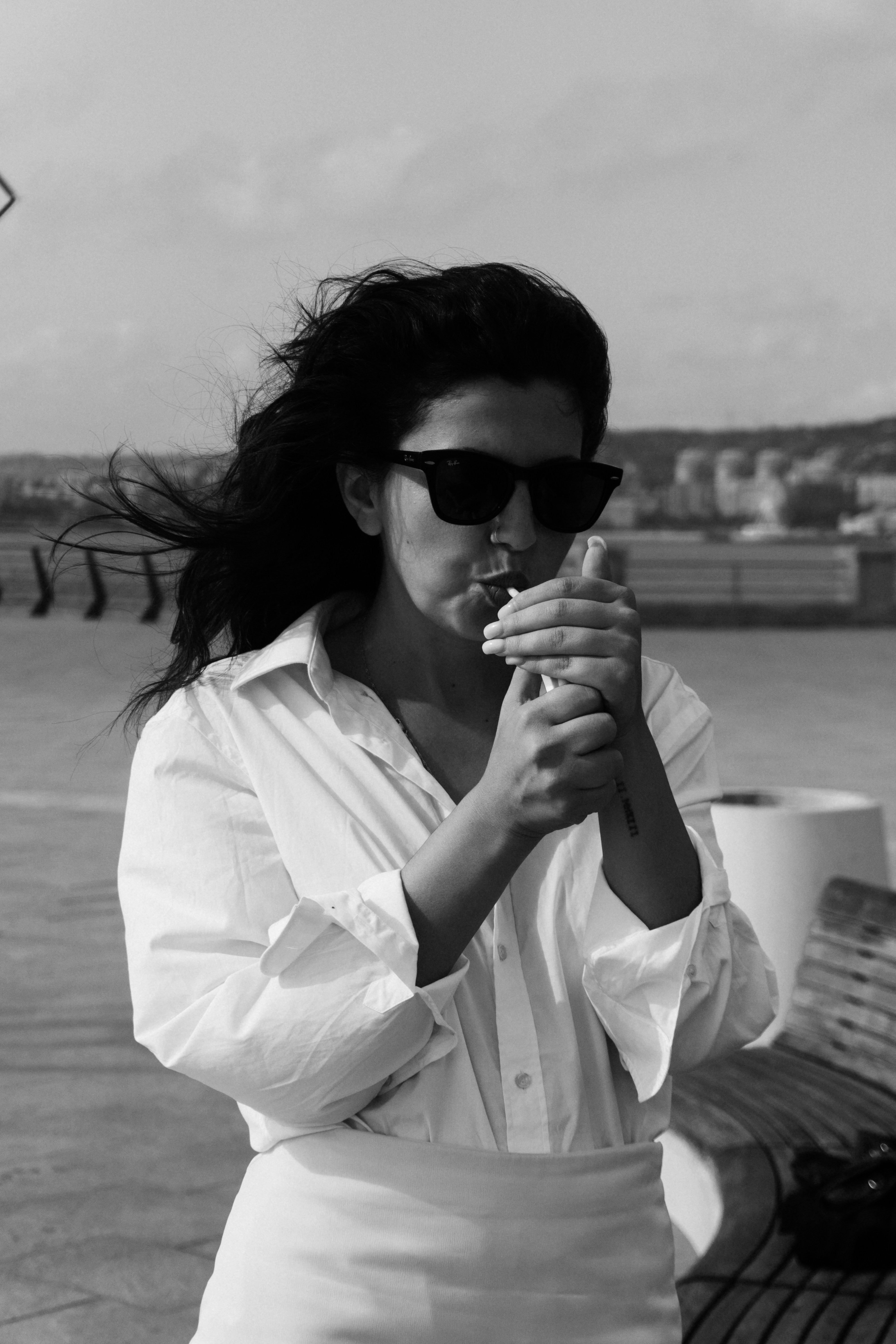 A woman in a white shirt lighting a cigarette outdoors in black and white