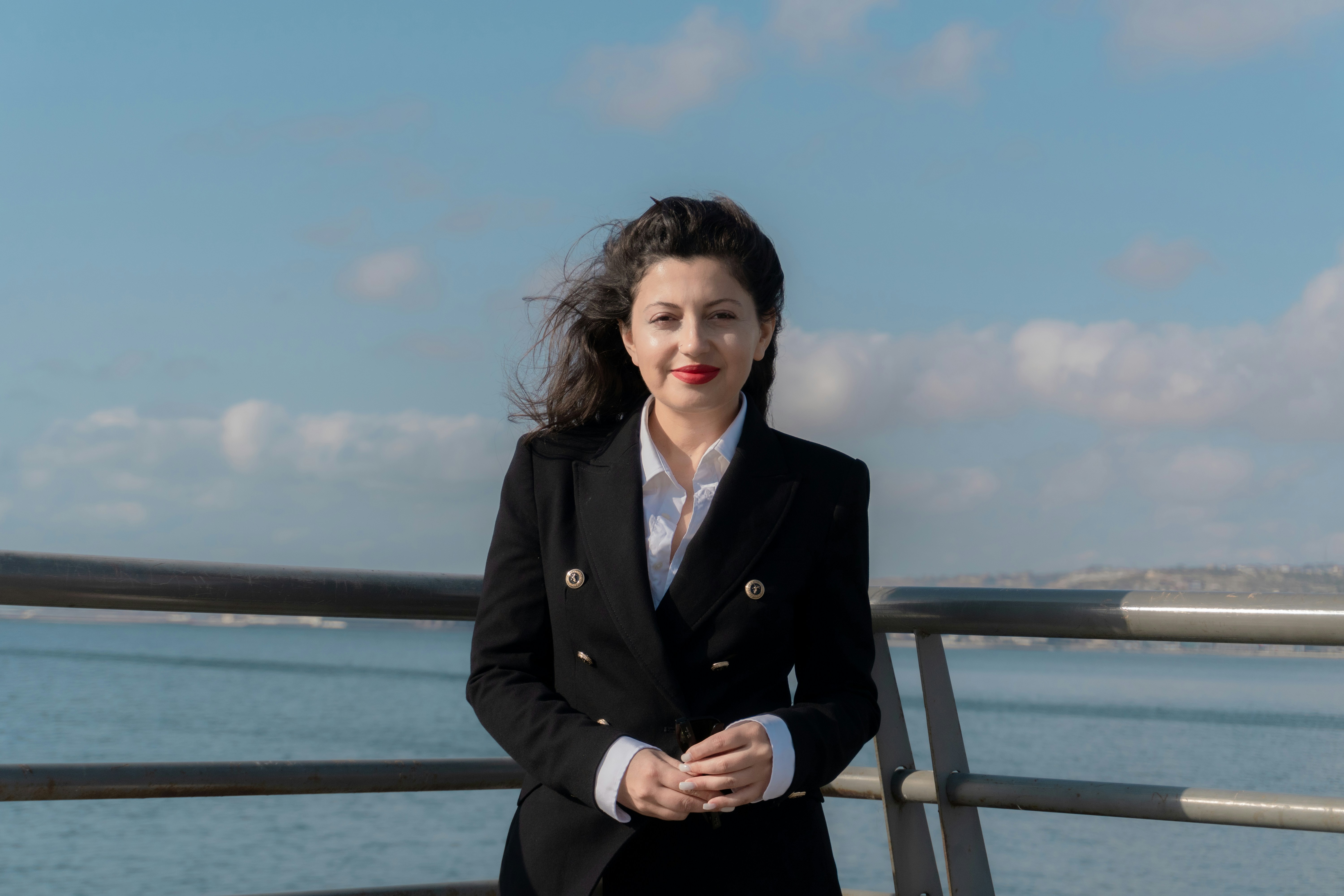 A woman in a black blazer and white shirt standing by a metal railing
