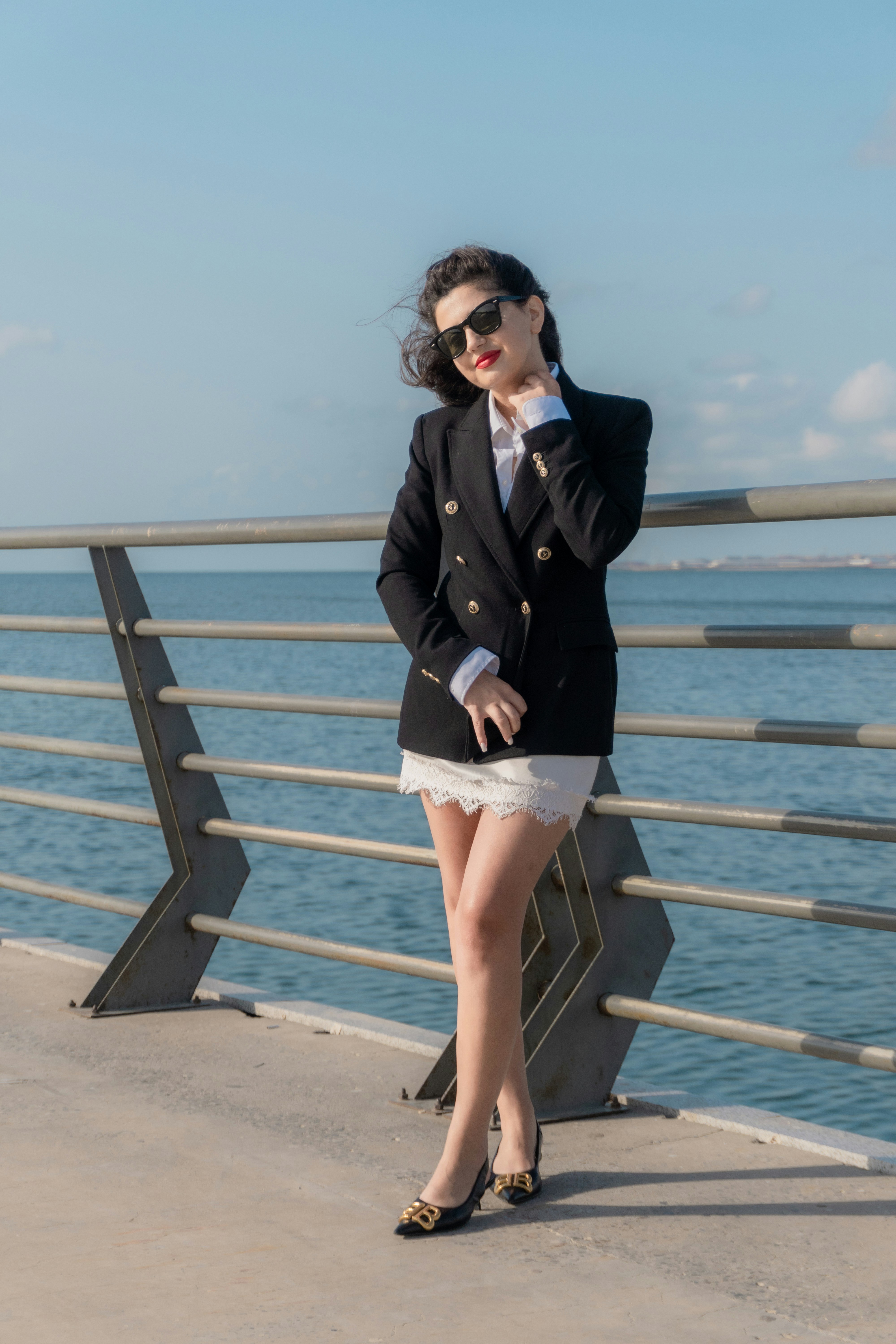 A woman in a black blazer and white skirt by a metal railing
