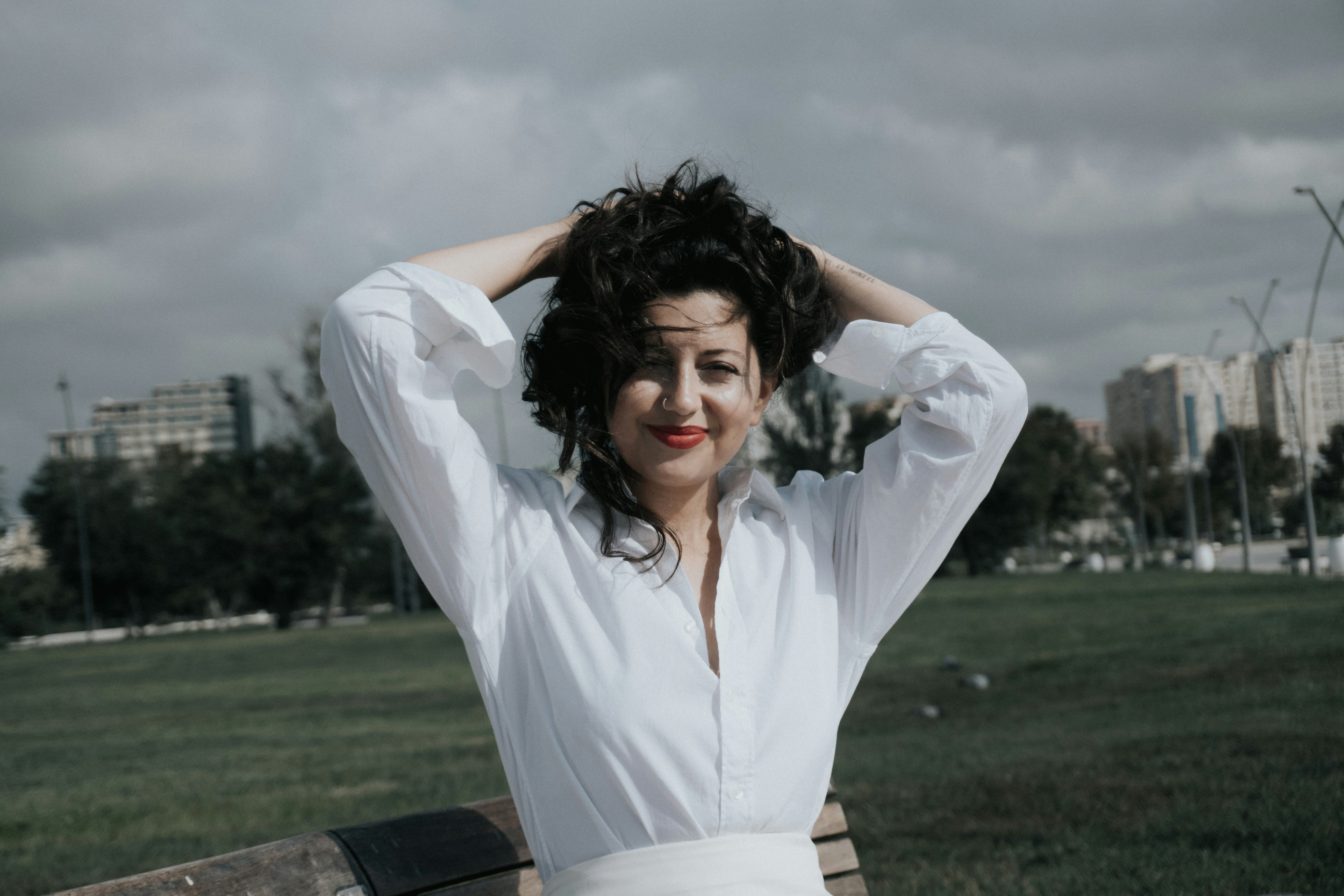 A woman in a white shirt holding her dark hair in a park