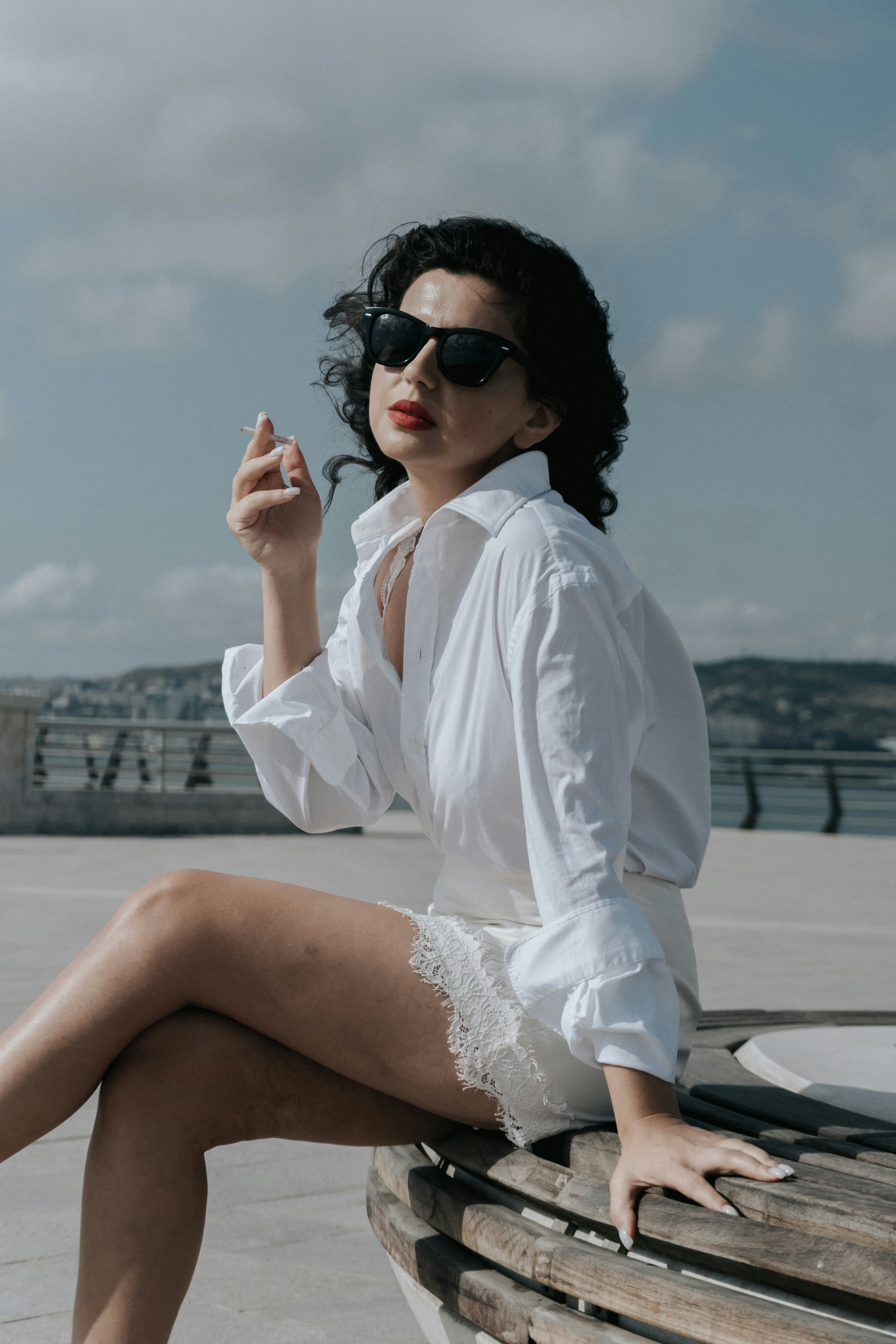 A woman in a white shirt and lace skirt holding a cigarette outdoors