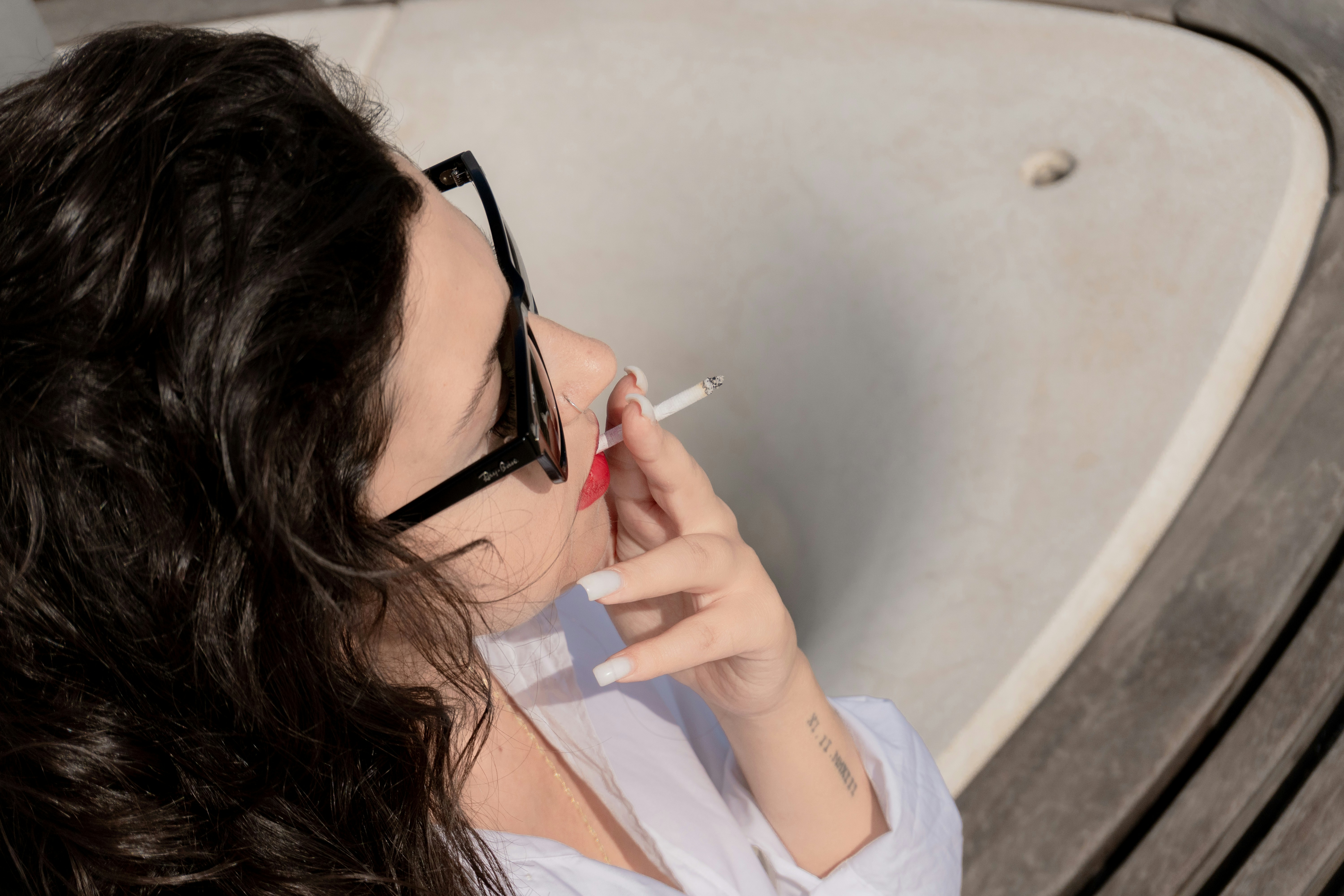 A woman with dark hair wearing black sunglasses holding a cigarette to her lips