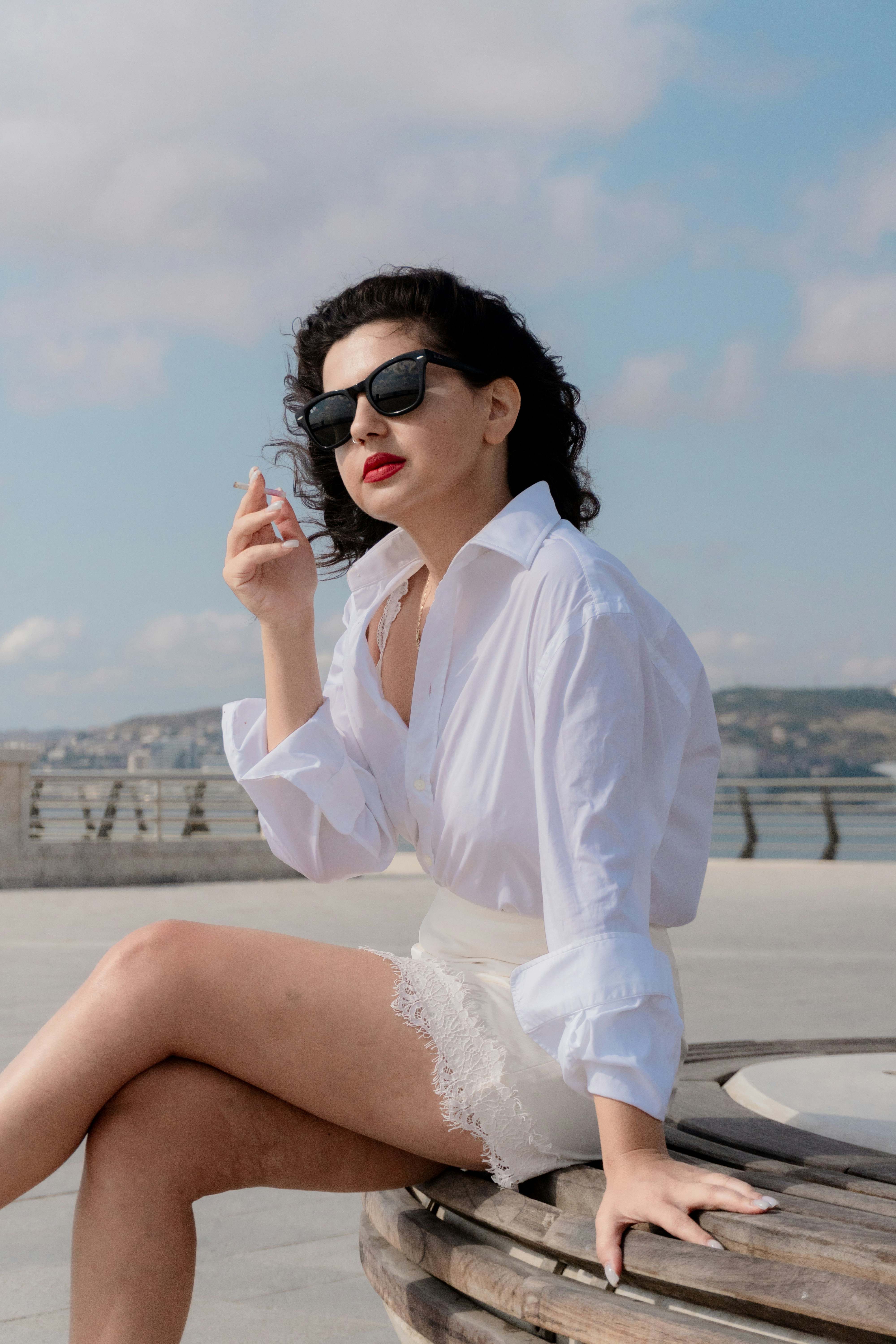 A woman in a white shirt and lace skirt holding a cigarette outdoors