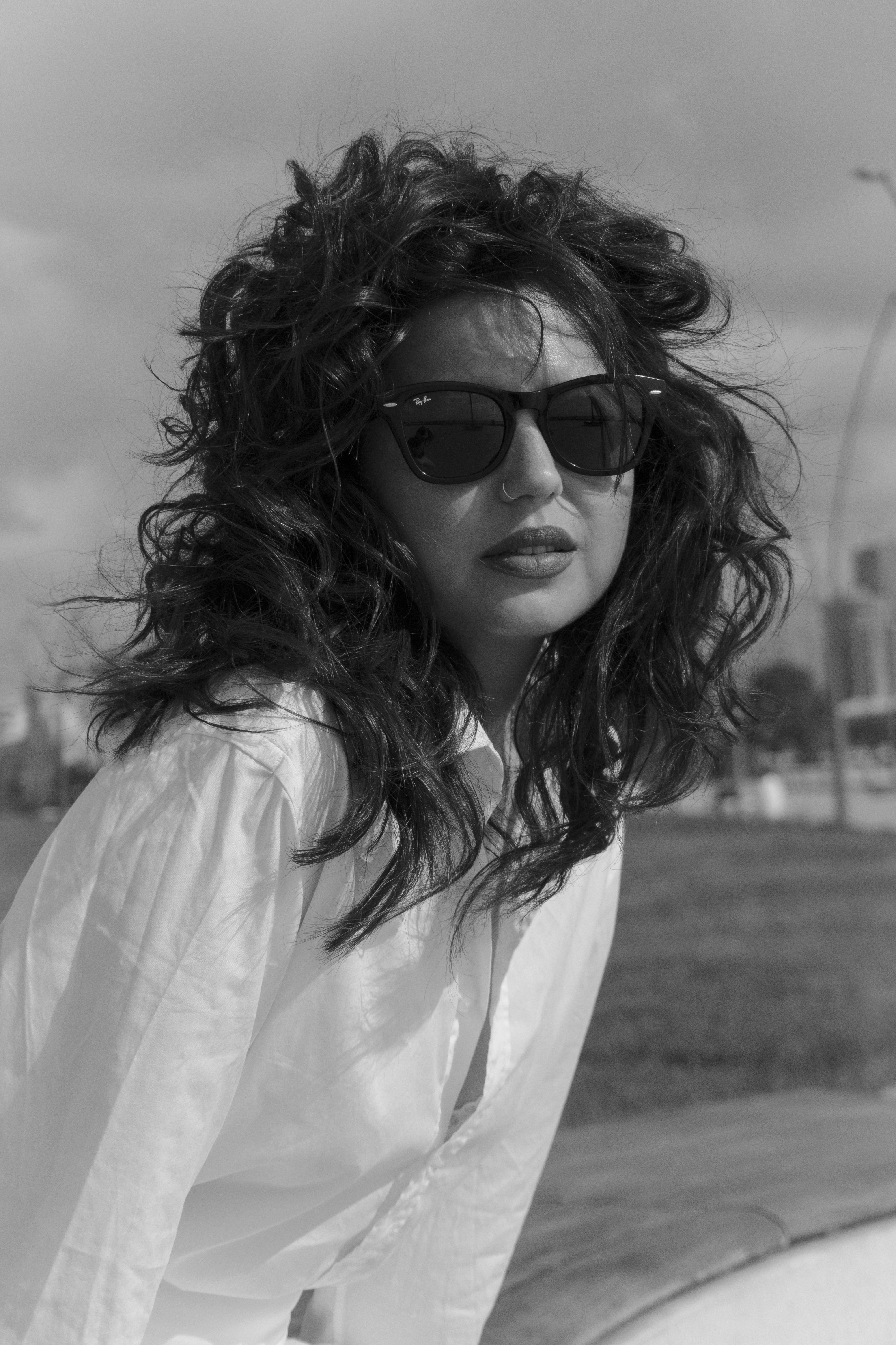 A woman with curly hair wearing sunglasses and a white shirt outdoors