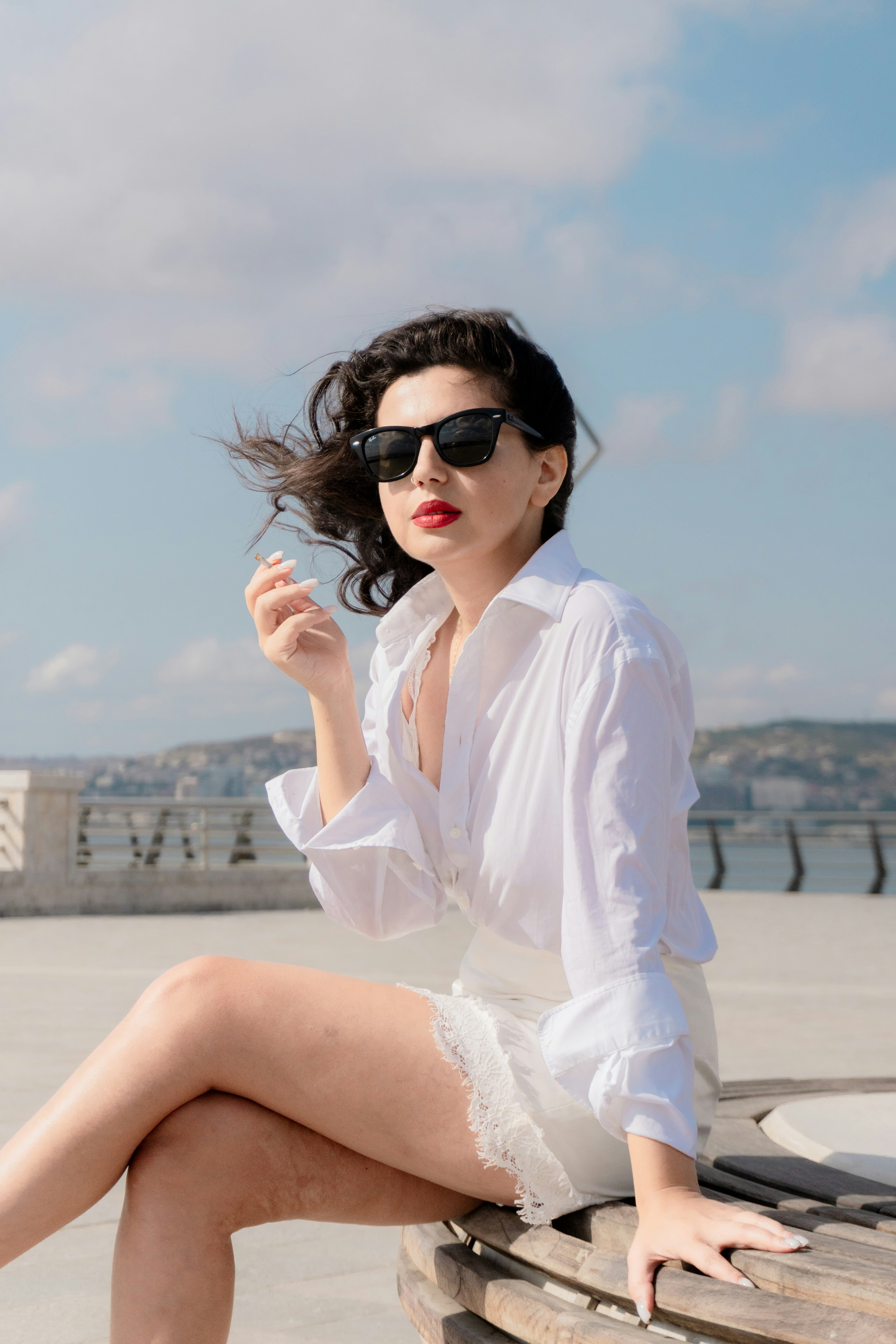 A woman in a white shirt and sunglasses sitting on a wooden bench
