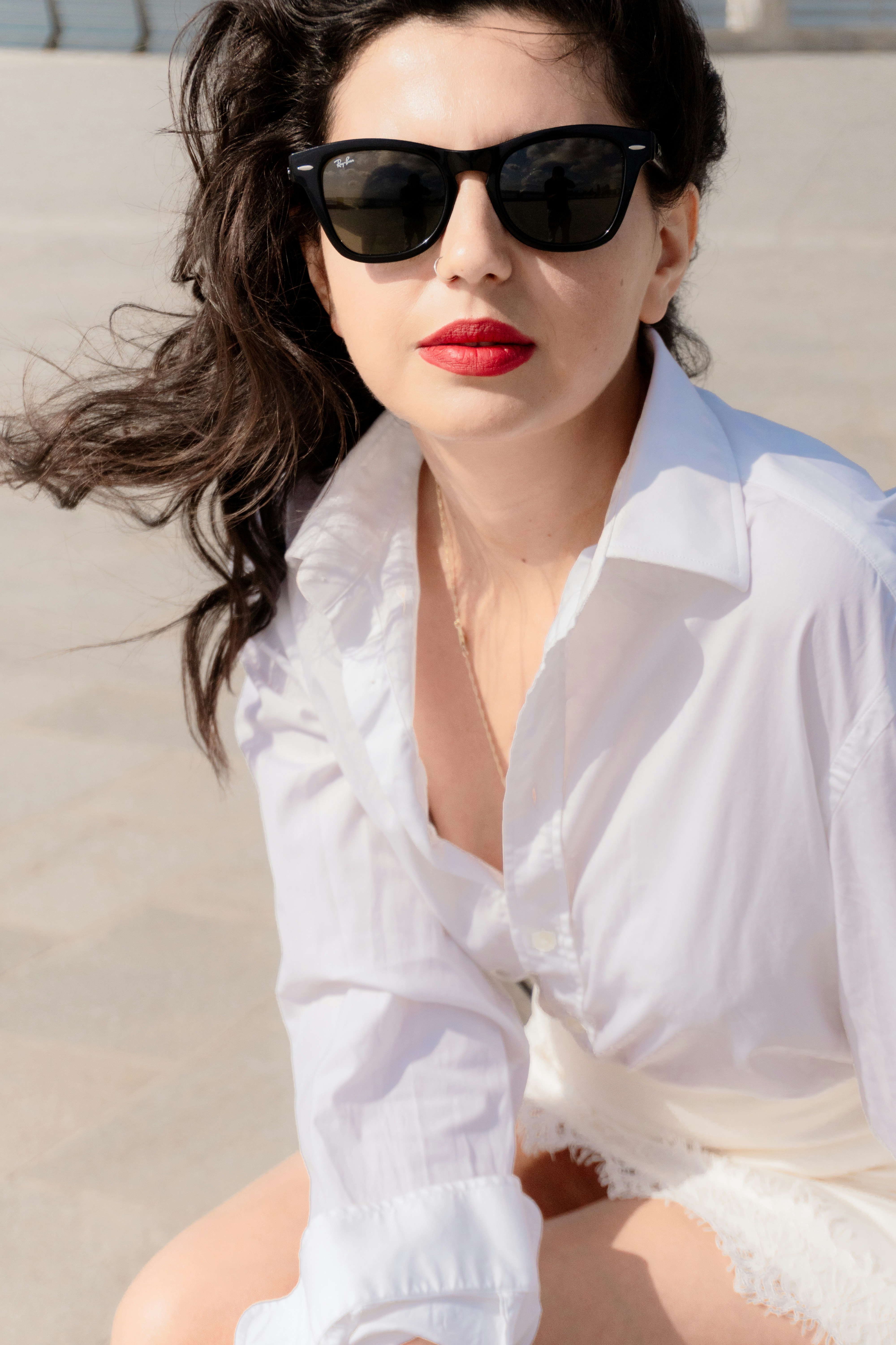 A woman with dark hair wearing black sunglasses and a white shirt outdoors