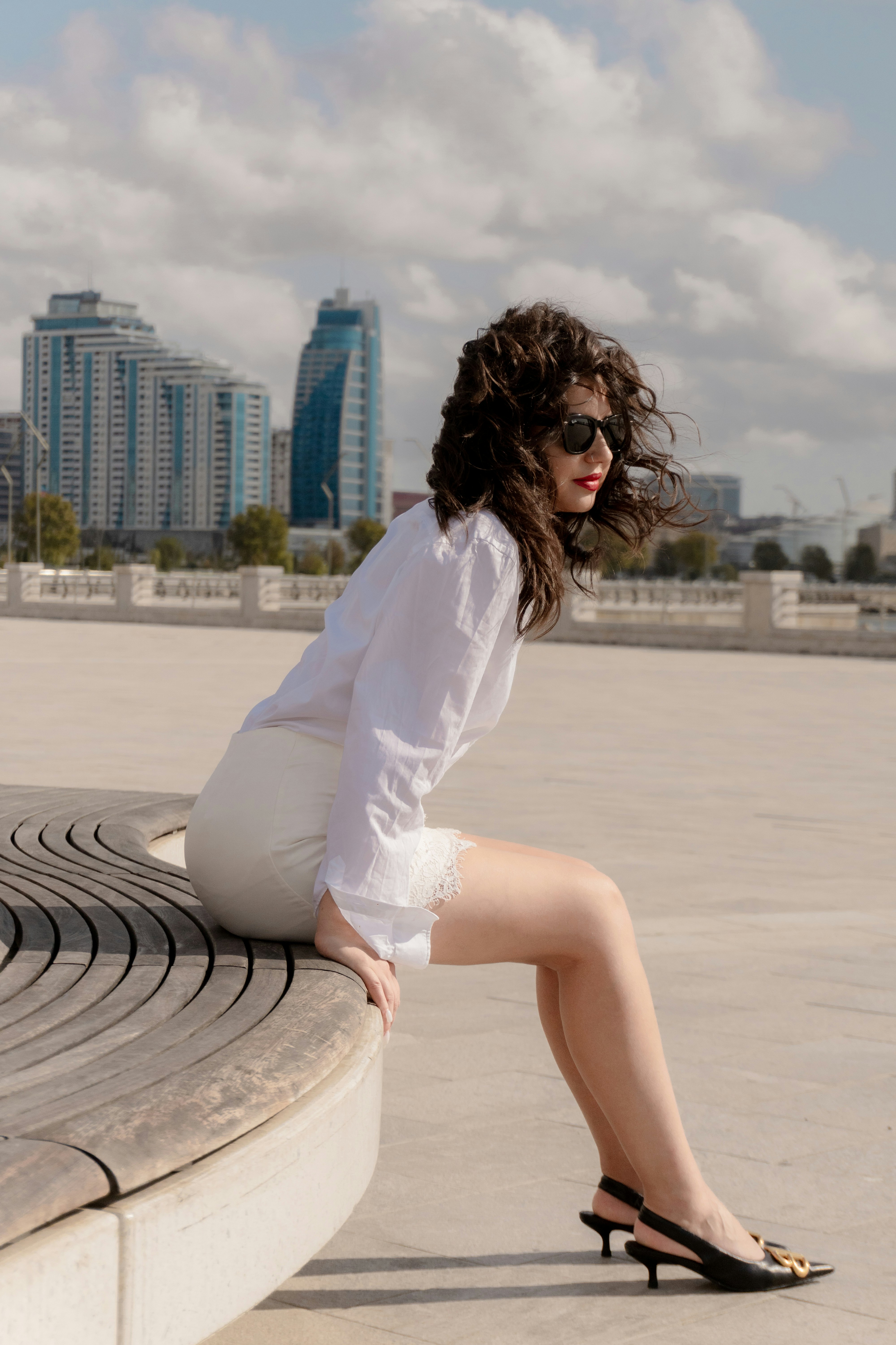 A woman in a white shirt and skirt sitting on a curved wooden bench