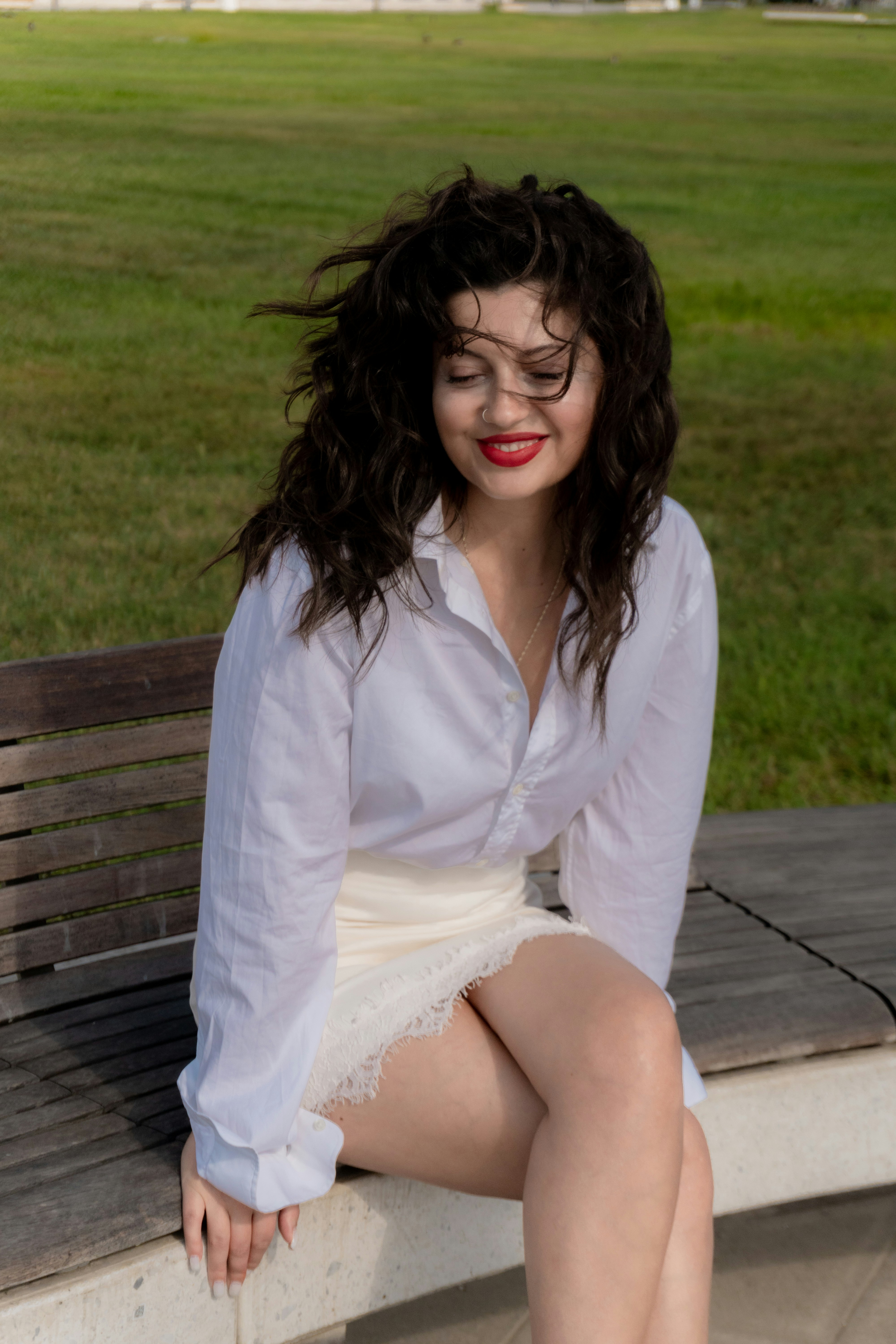 A woman with dark curly hair in a white shirt on a wooden bench