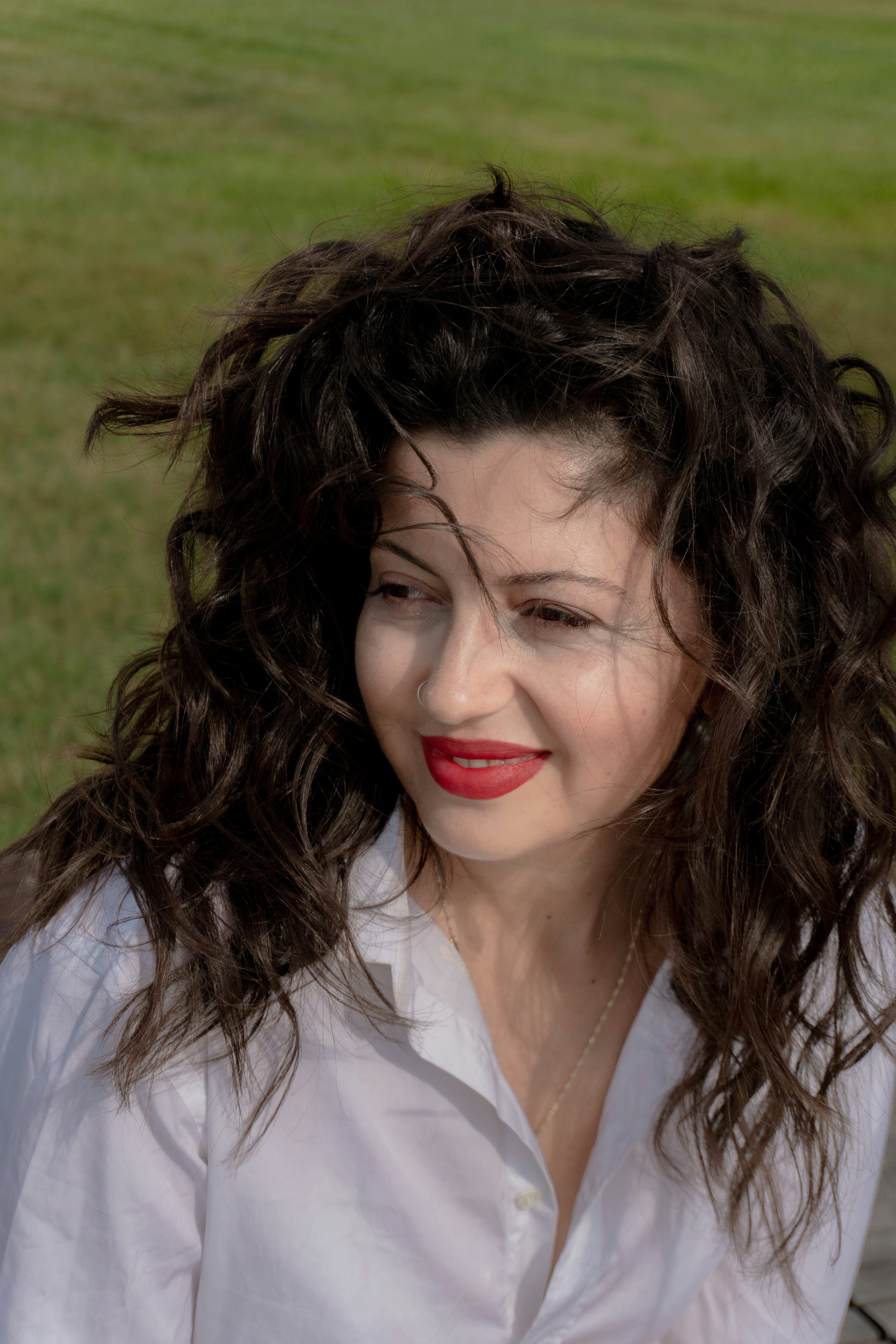 A woman with long curly dark hair and red lipstick in a white shirt