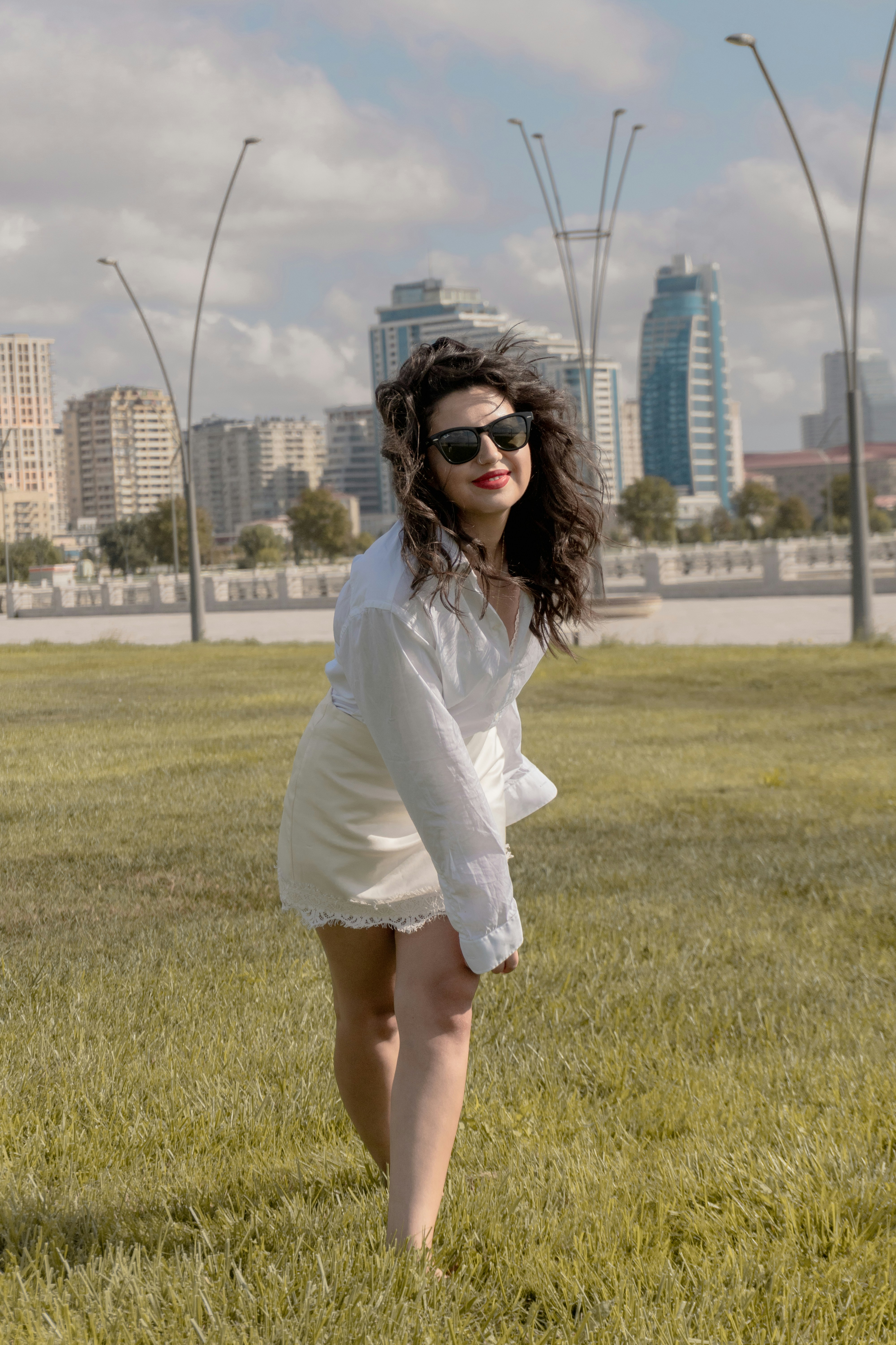 A woman in a white shirt and skirt on a grassy field in Baku
