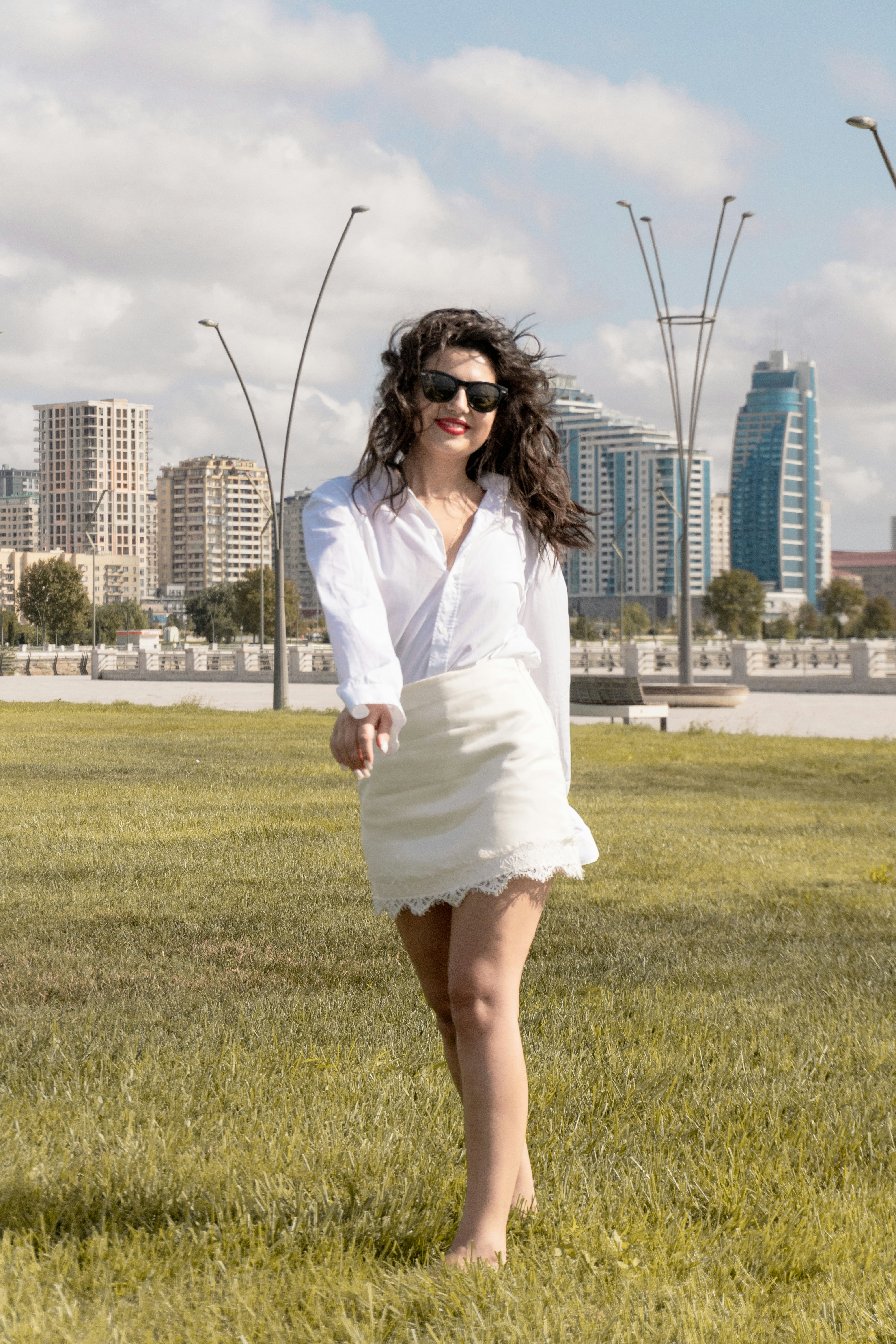 A woman in a white shirt and skirt walking through a grassy park